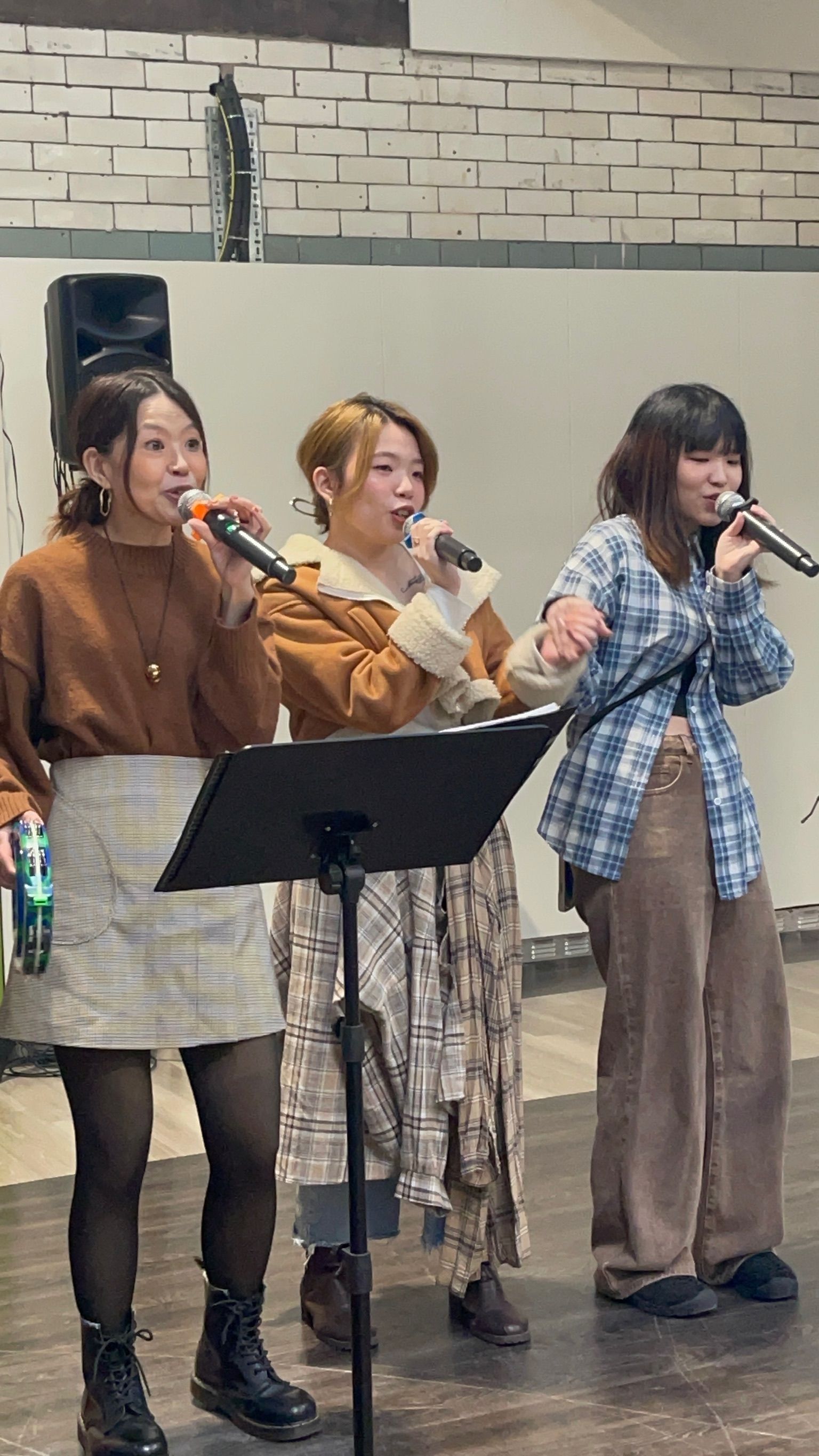Three women singing into microphones on stage.