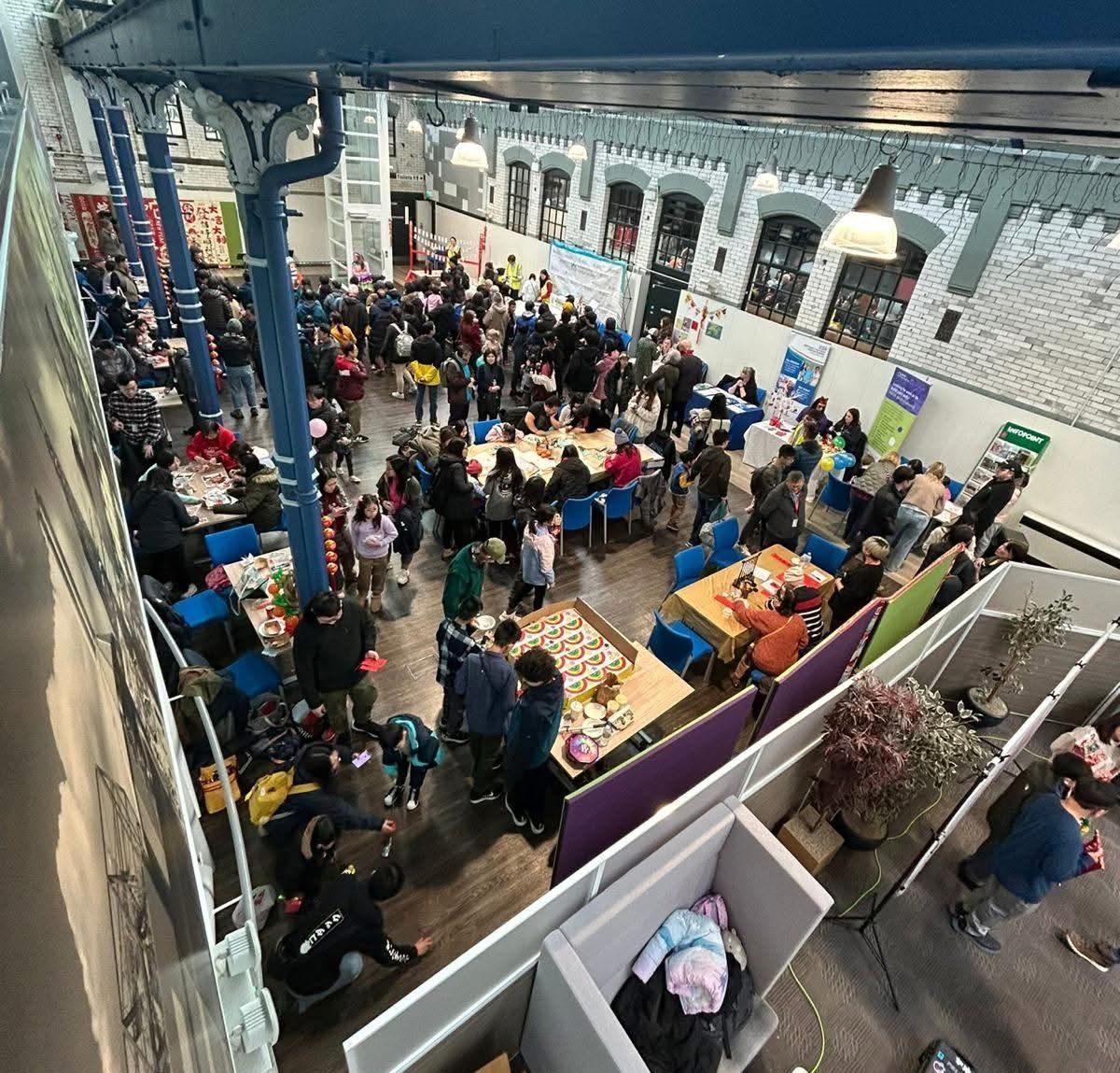 Large event inside a brick building. People gather around tables, likely at a market or fair.