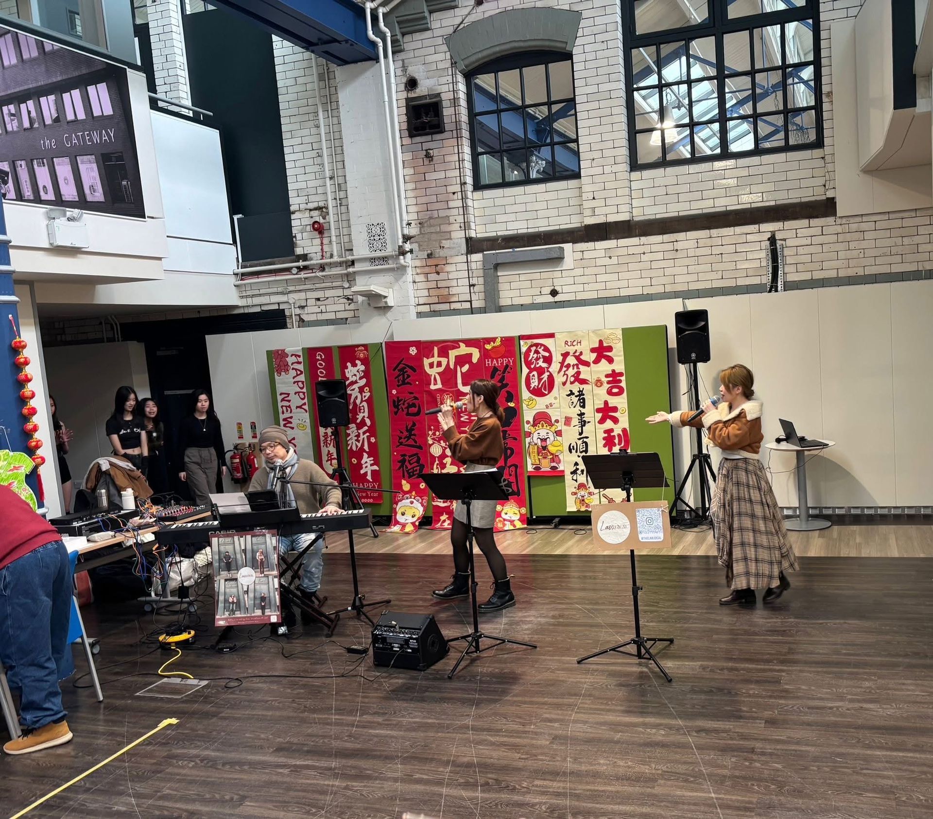 A performance with musicians on stage in a brightly lit room. Banners and audience in the background.