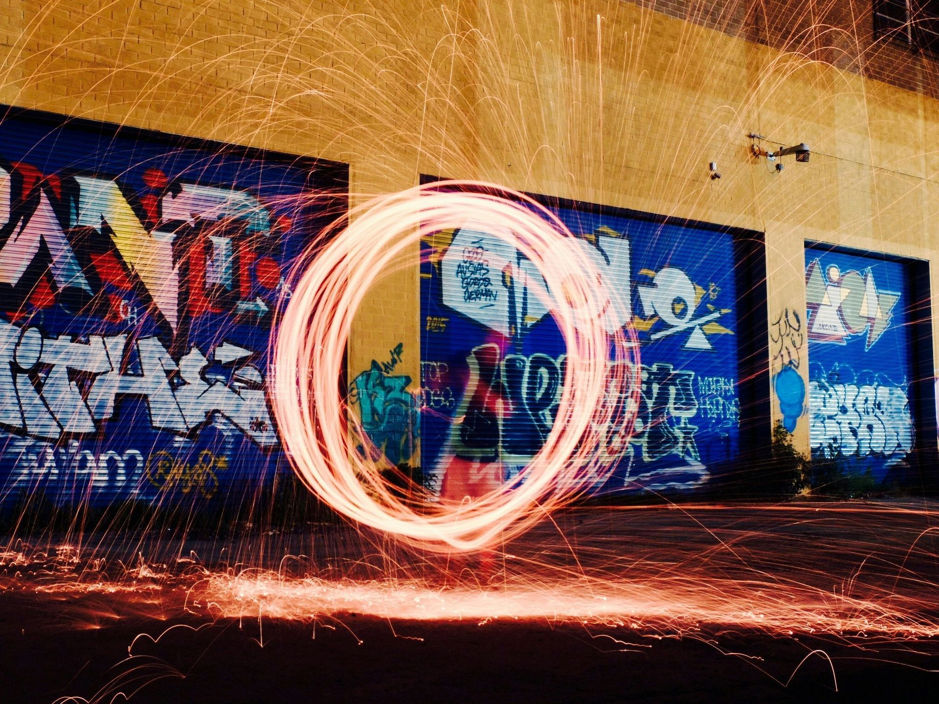 A fiery circle created by steel wool sparks against a graffiti-covered wall at night.