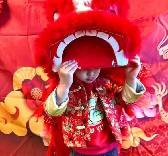 Child in red lion dance costume, holding up the head, celebrating Lunar New Year.