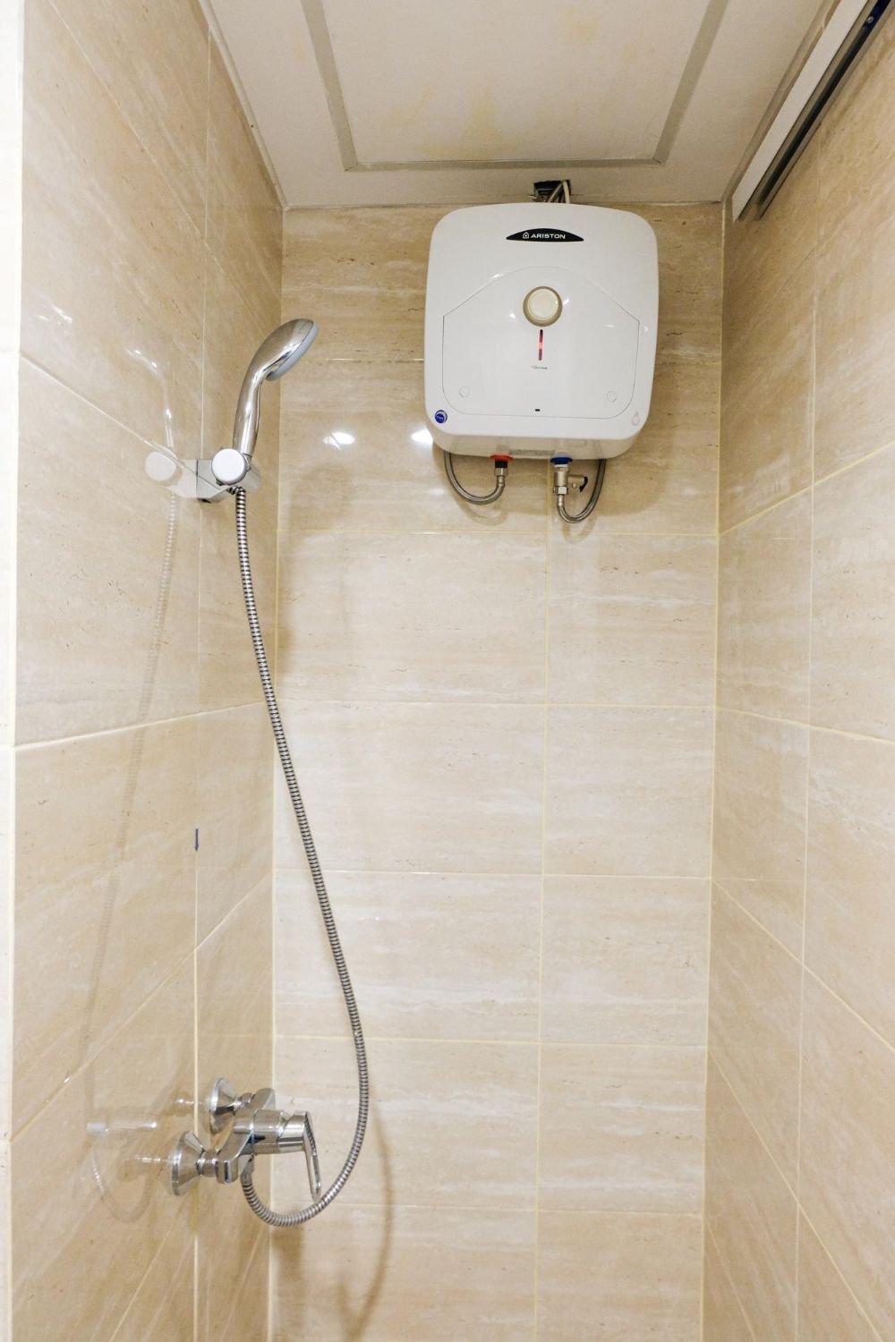 A small bathroom shower with beige tiles, a wall-mounted water heater, and a showerhead.