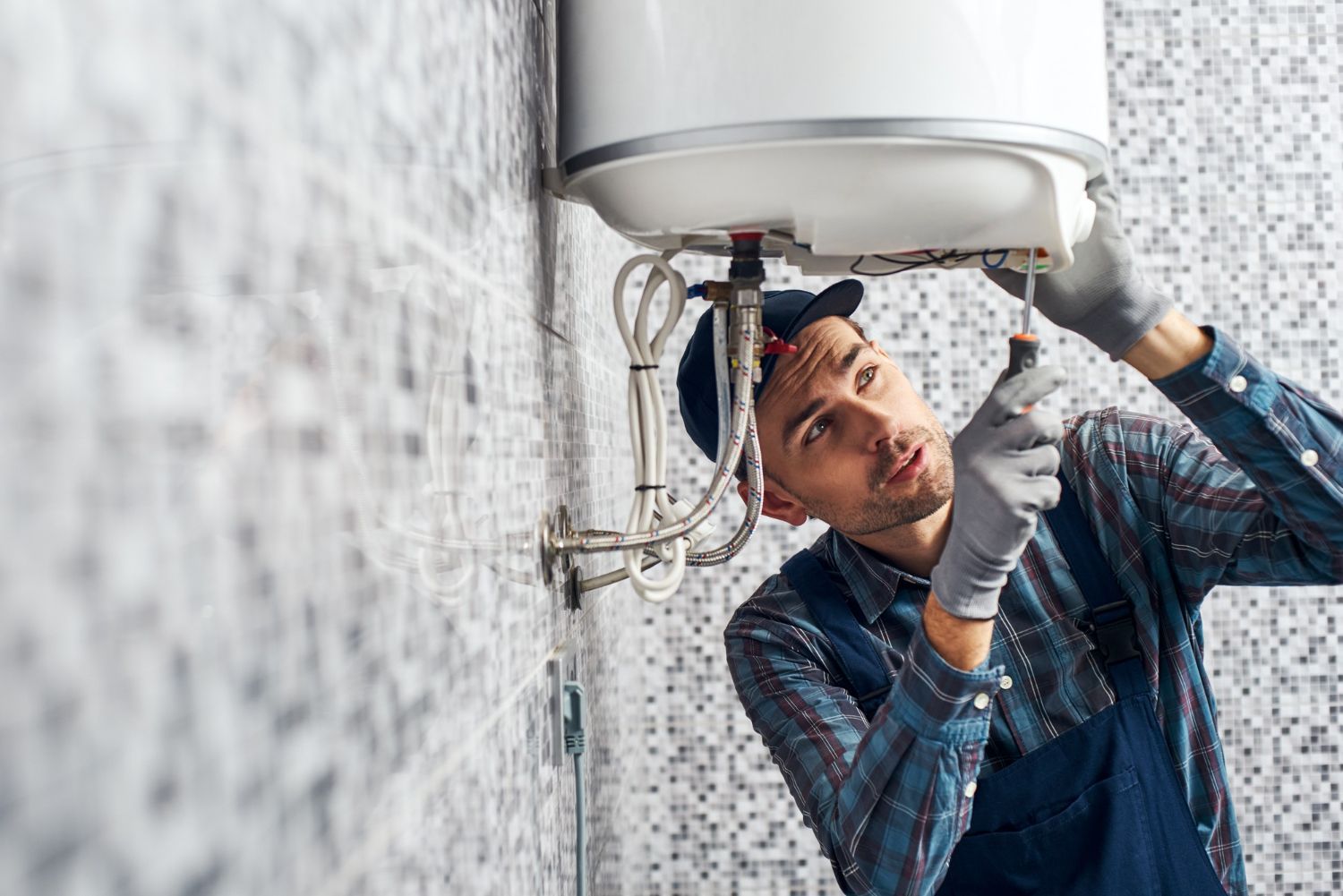 Plumber installing a hot water heater in a tiled bathroom; using a screwdriver.