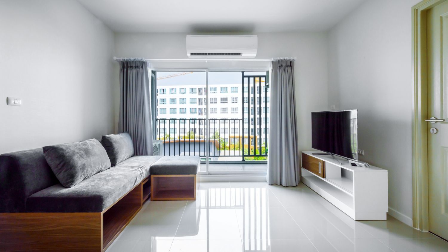 Living room with gray sofa, white TV stand, and large window overlooking a building.