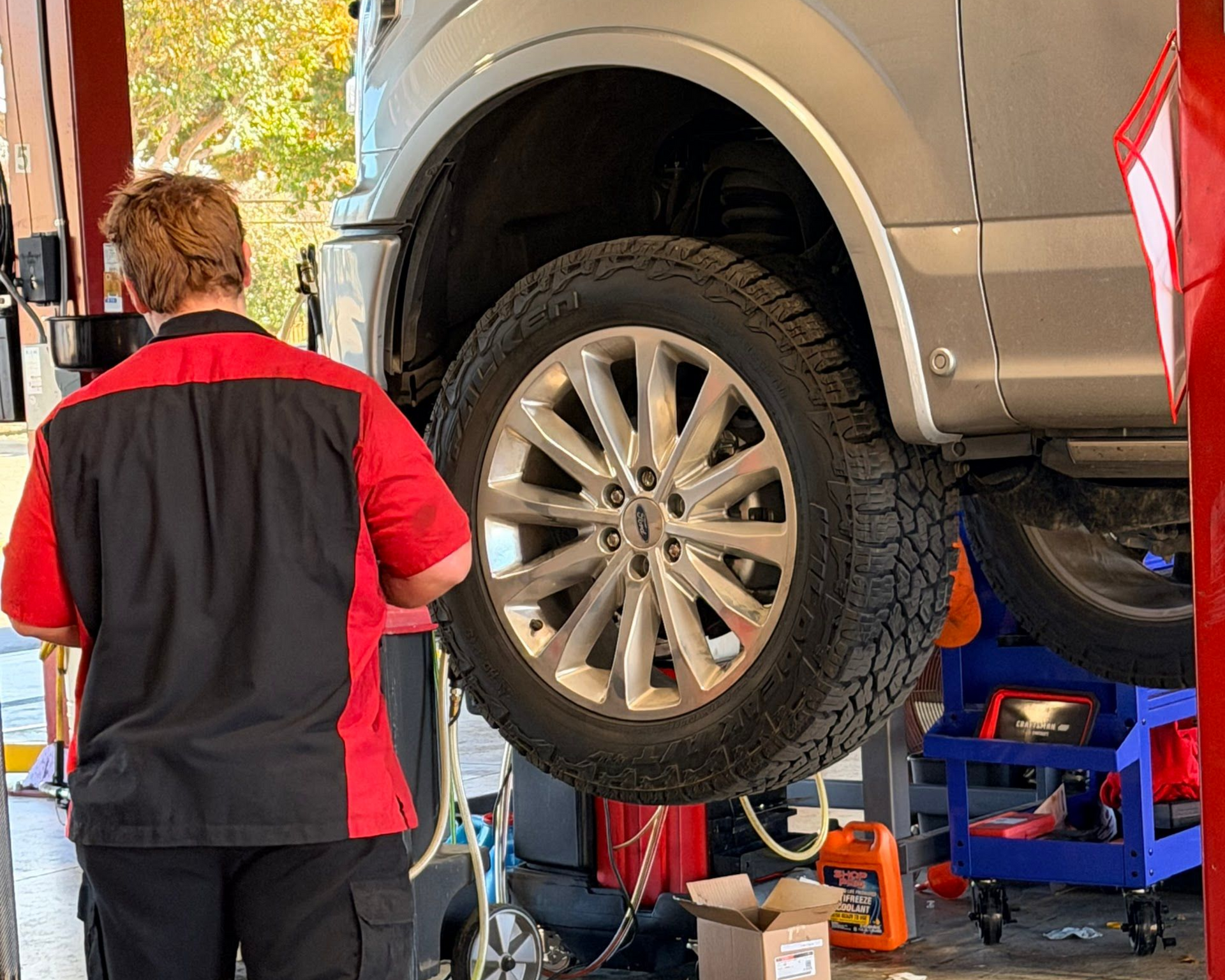 Mechanic working under a lifted silver SUV in an auto repair shop