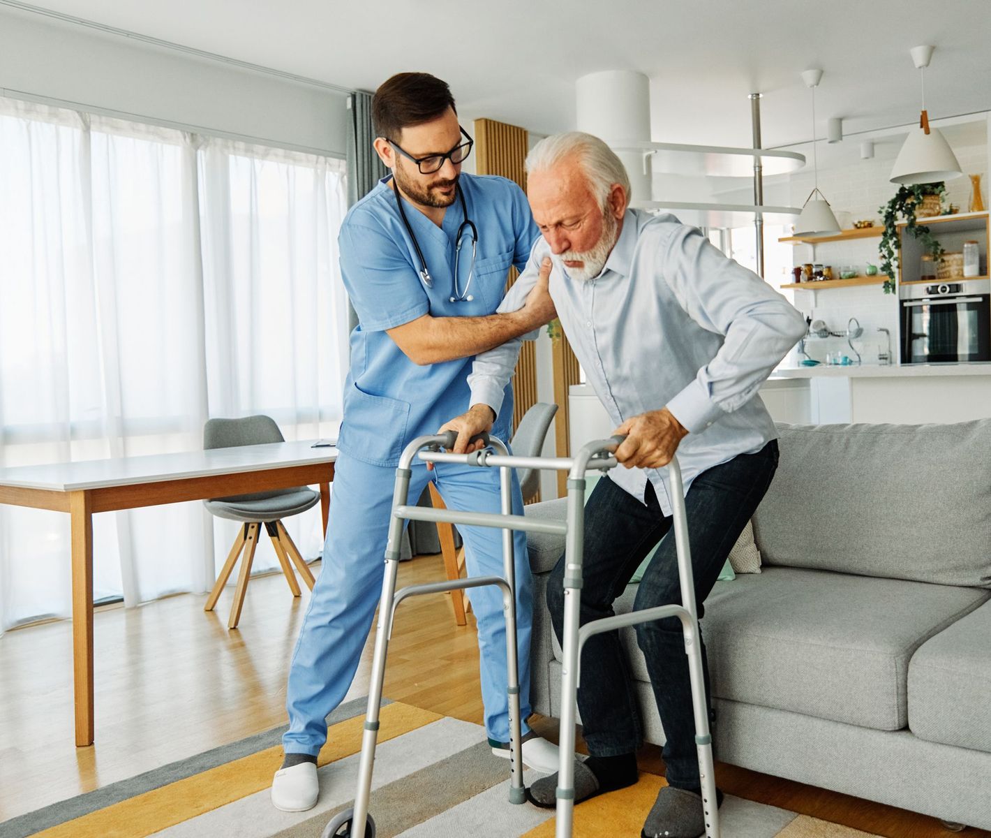 A nurse is helping an elderly man use a walker in a living room.