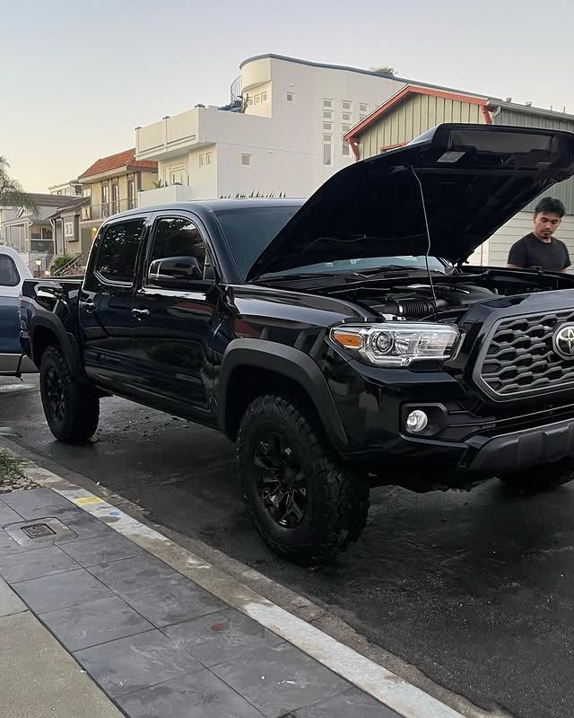 A black truck with the hood up is parked on the side of the road.