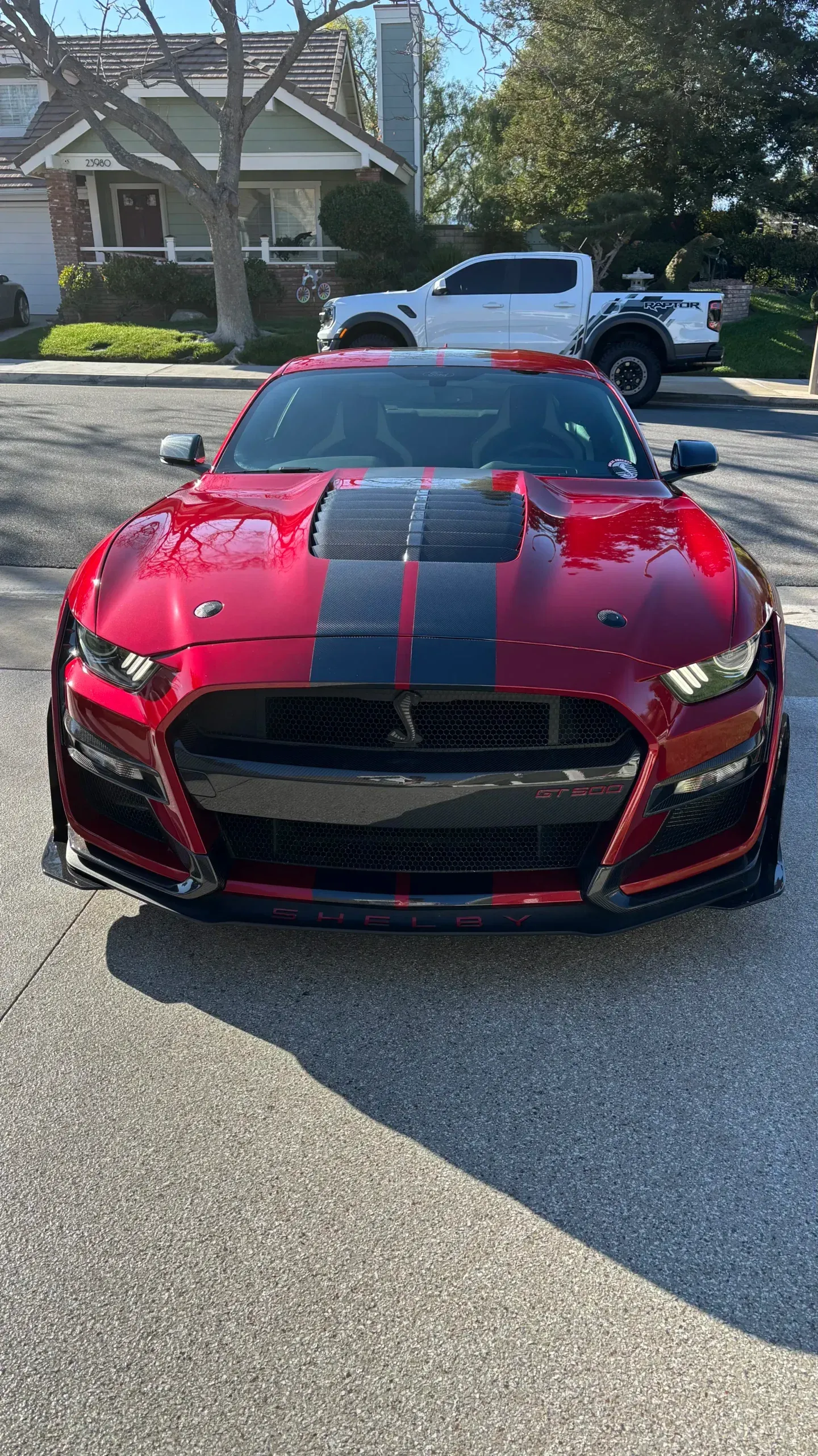A red mustang is parked on the side of the road in front of a house.