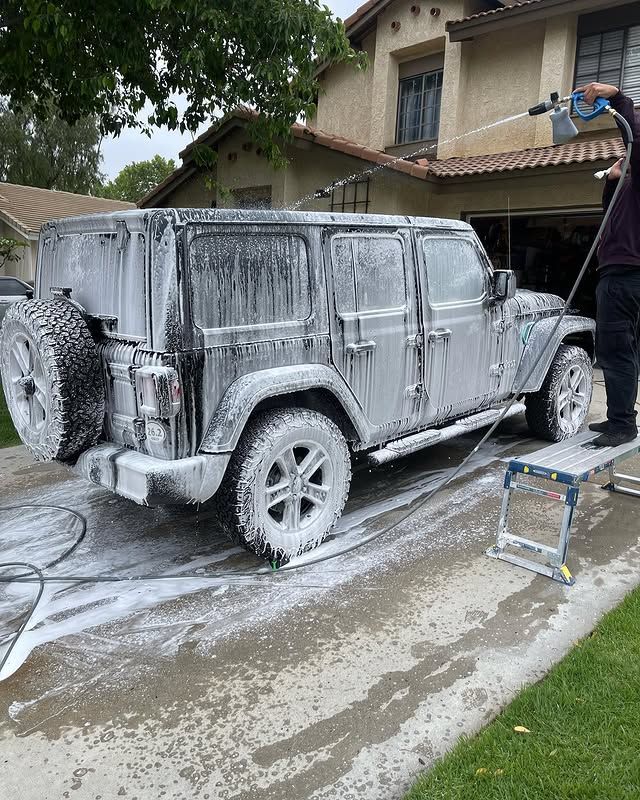 A man is washing a jeep with foam in front of a house.