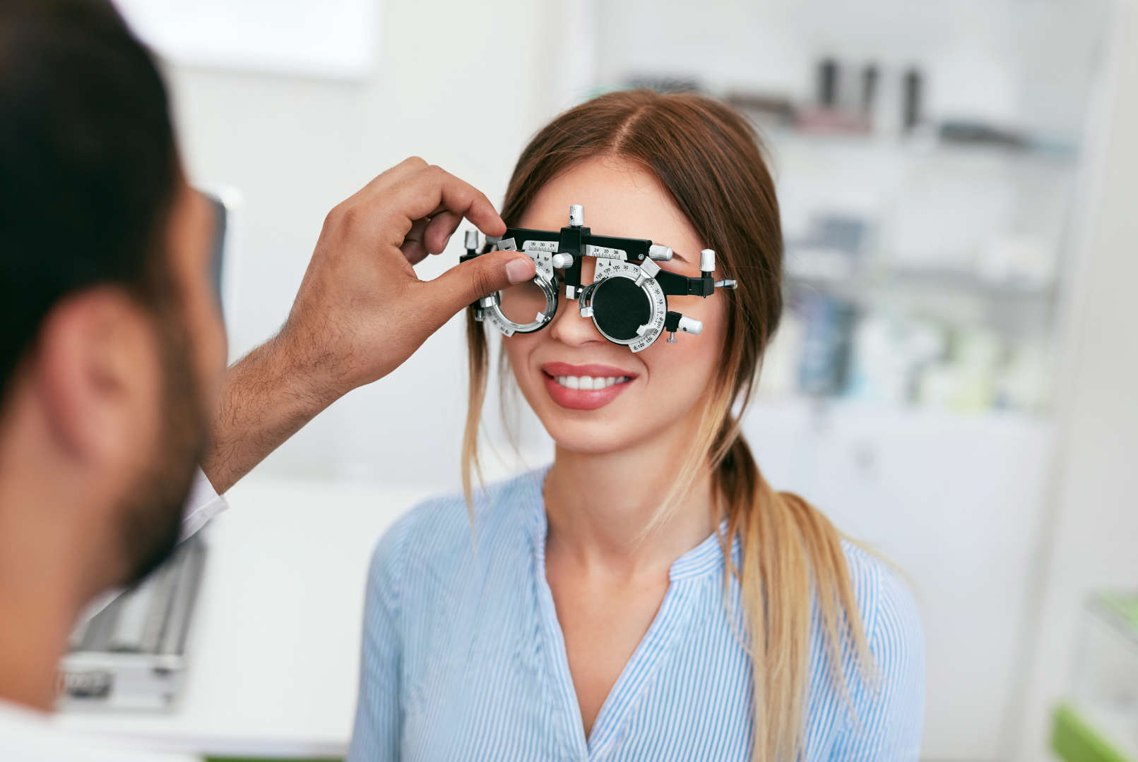 Optometrist adjusting trial lenses on a smiling patient in a bright exam room