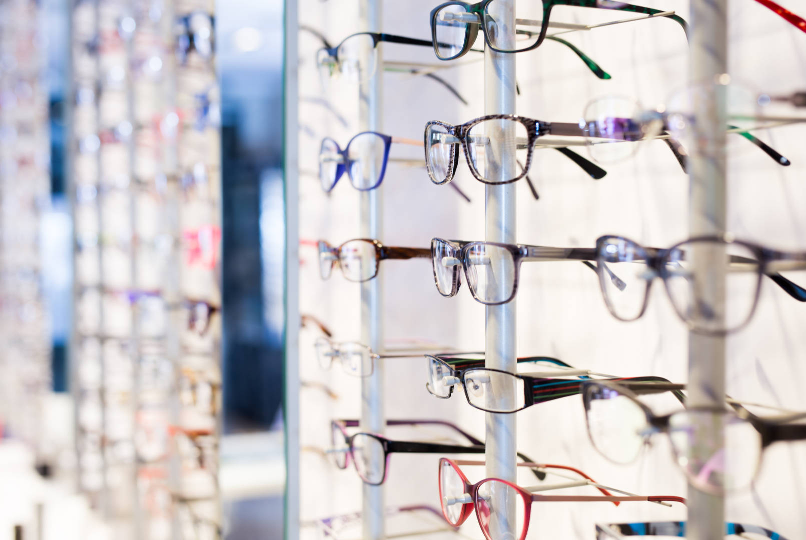 Rows of eyeglasses displayed on a store rack, with colorful frames in the background