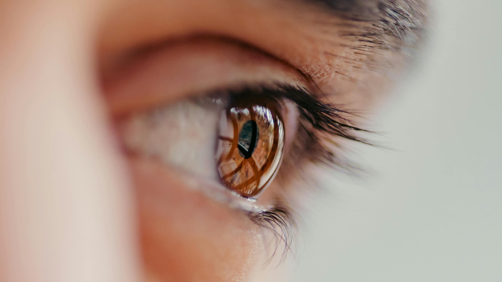 Close-up of a brown eye reflecting warm light, framed by eyelashes and a blurred face background
