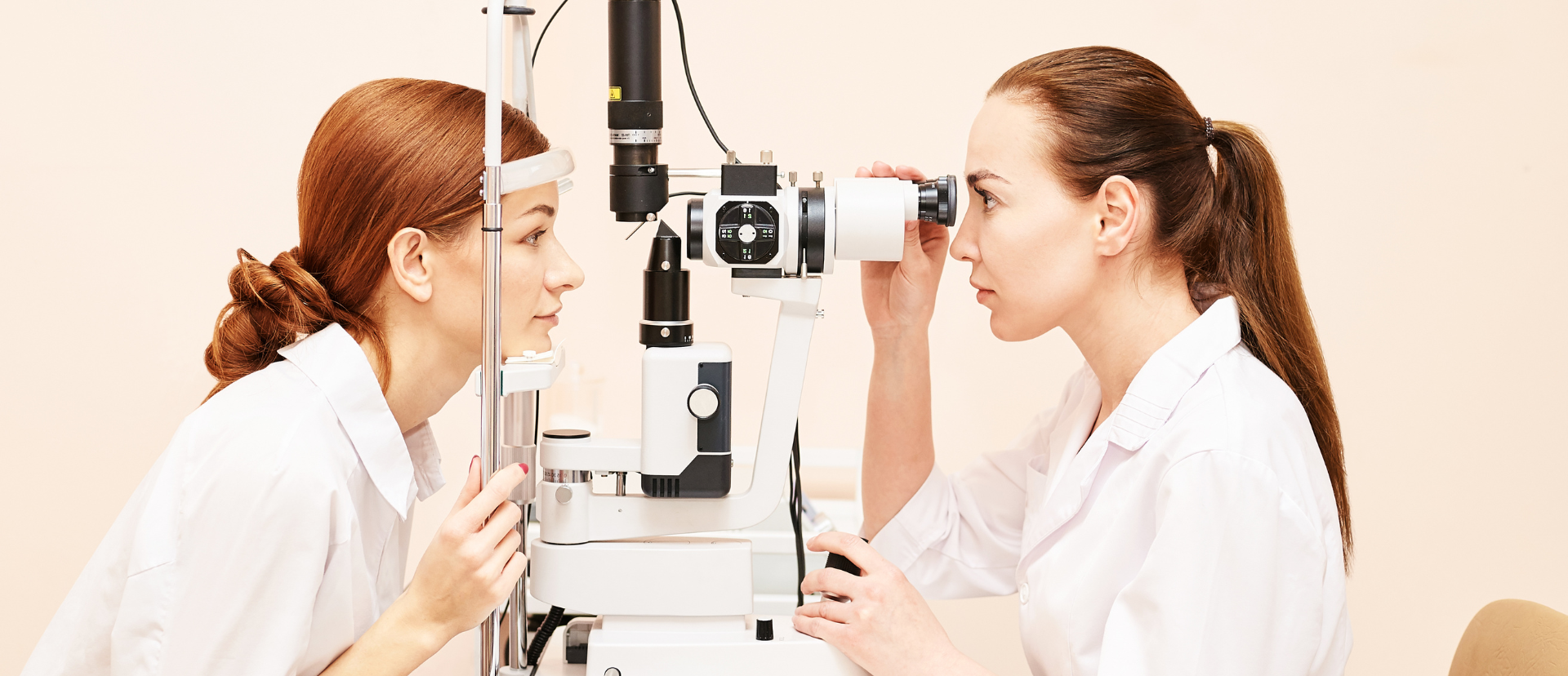 Two women in white coats examining eyes with a slit lamp at an eye clinic