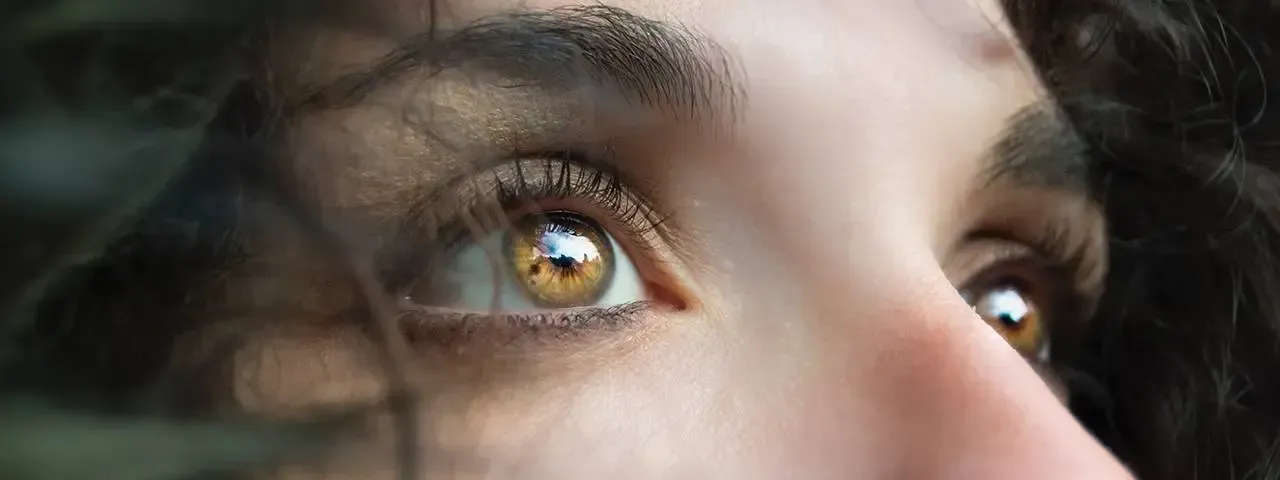 A close-up of a person's hazel-colored eyes looking upward, framed by dark hair and eyelashes.
