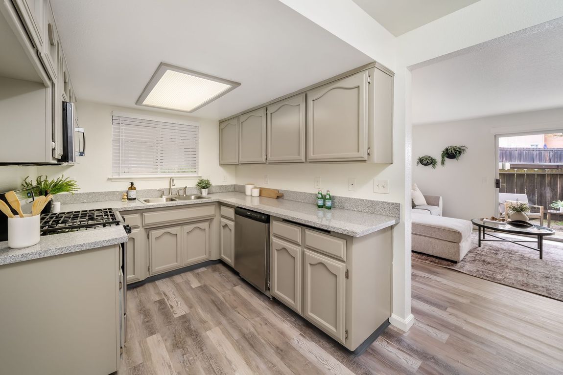 A kitchen with white cabinets , a stove , a sink , and a dishwasher.