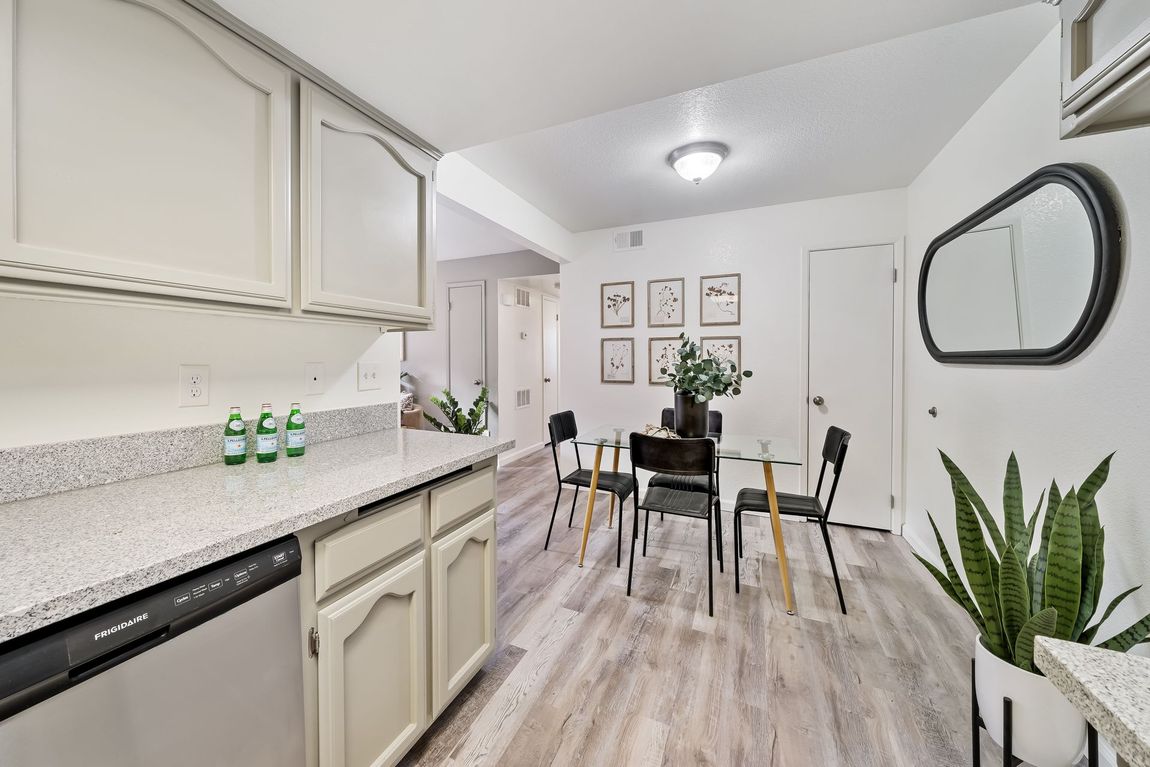 A kitchen with white cabinets and stainless steel appliances and a dining room with a table and chairs.