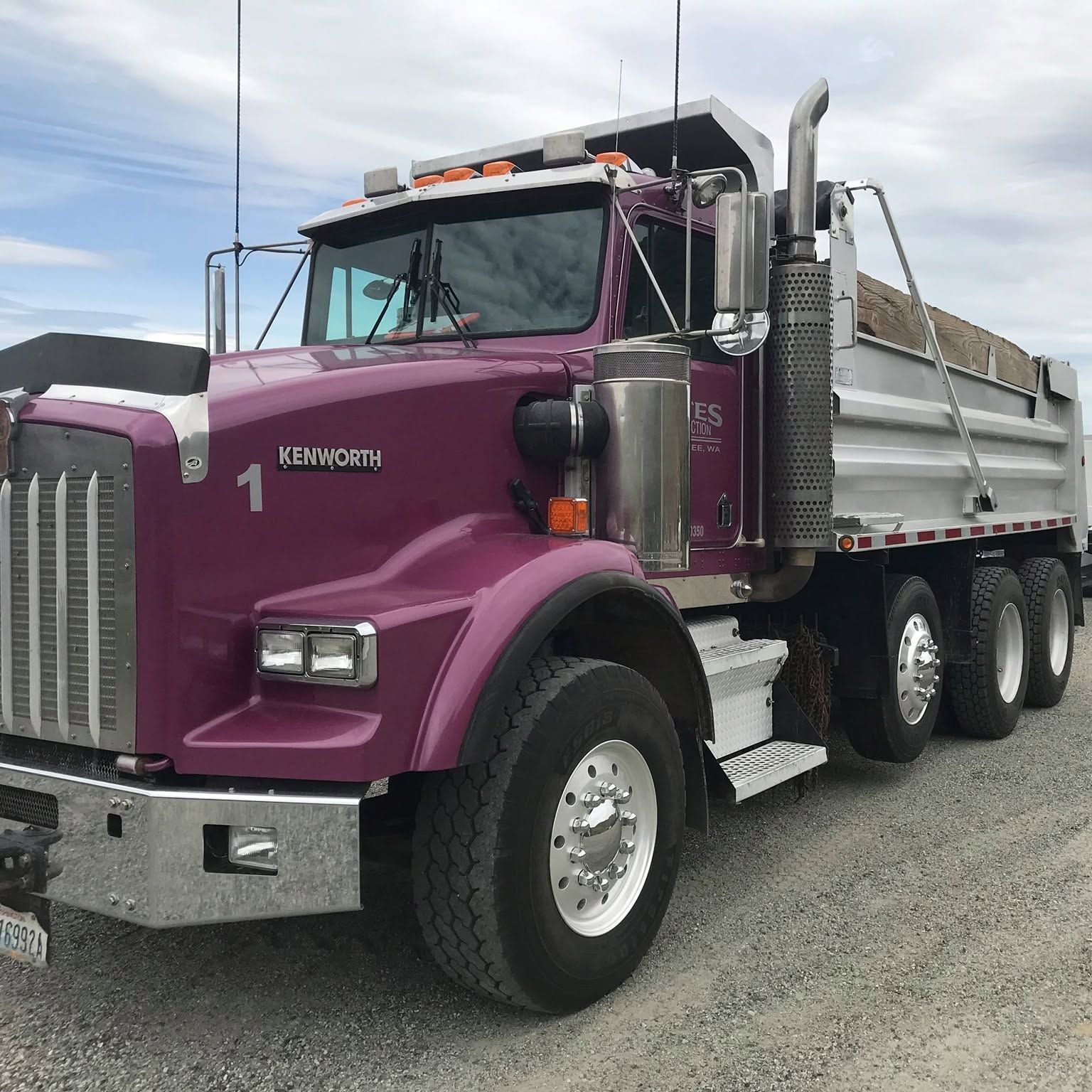 Purple Kenworth dump truck parked on gravel lot under cloudy sky