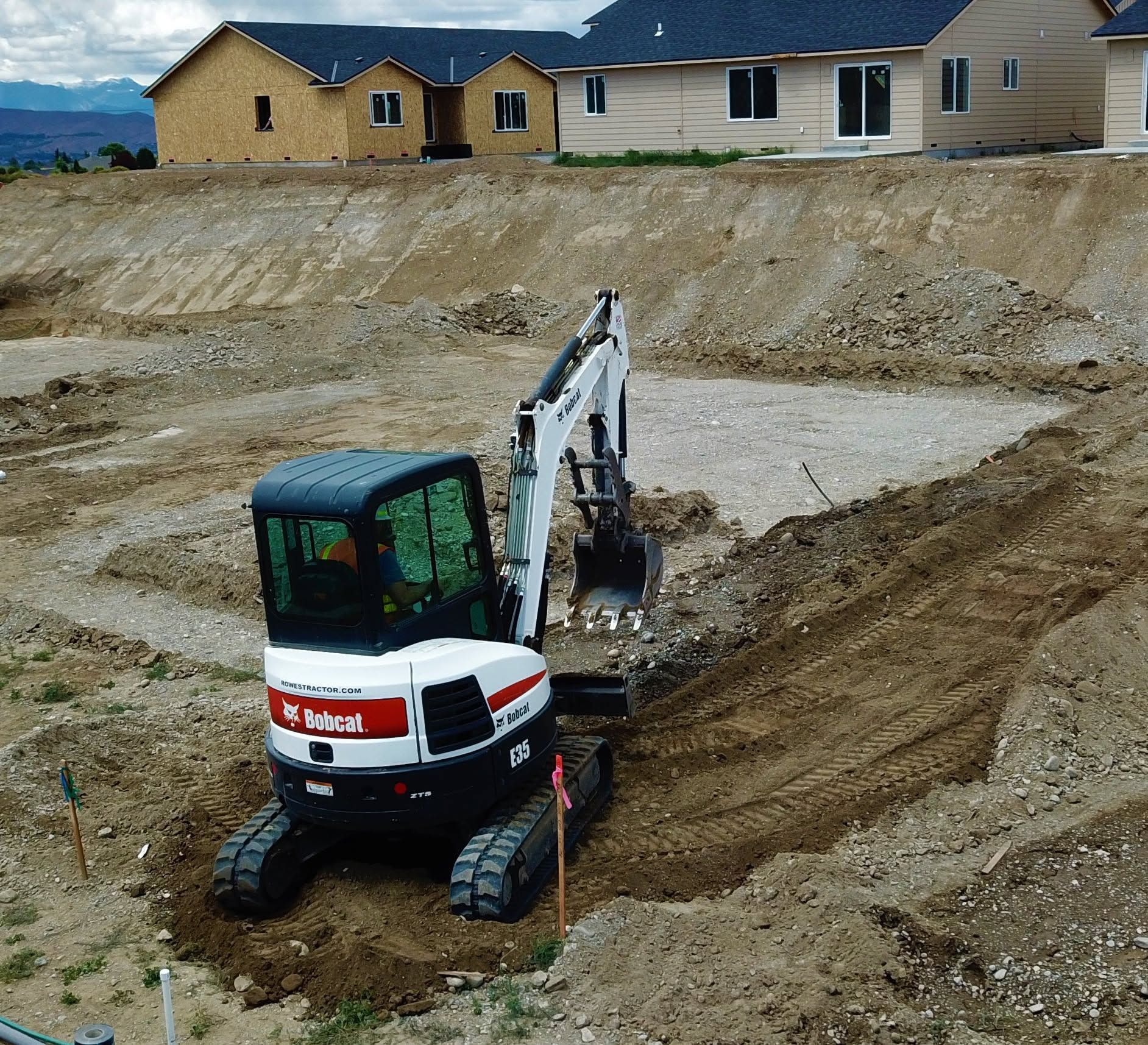 Mini excavator digging a trench on a dirt construction site near new houses