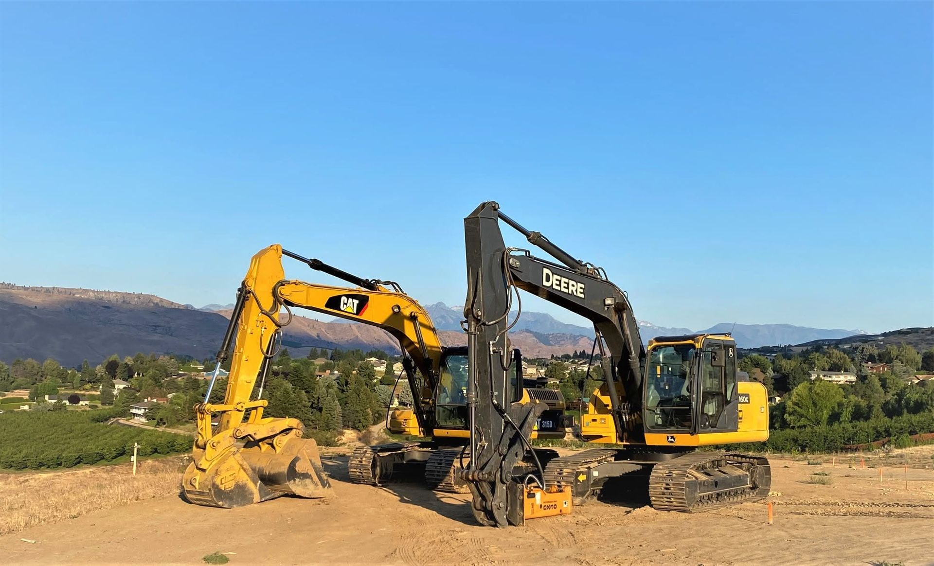 Two excavators, one yellow and one black, digging at a construction site under a clear blue sky.