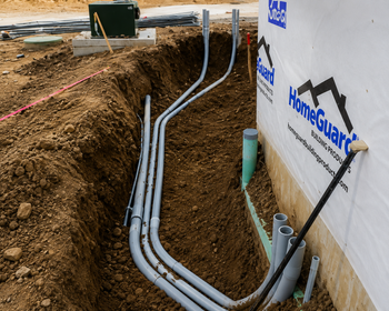 Underground utility conduits in a trench beside a HomeGuard foundation wall at a construction site