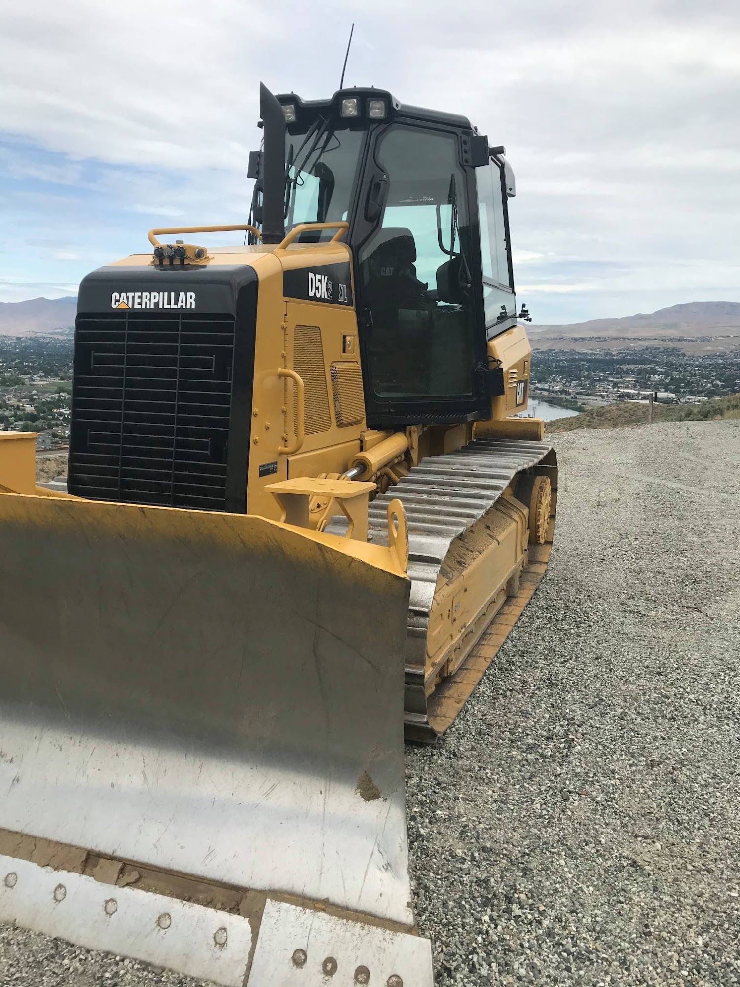 Yellow Caterpillar bulldozer parked on a gravel hill overlooking a valley