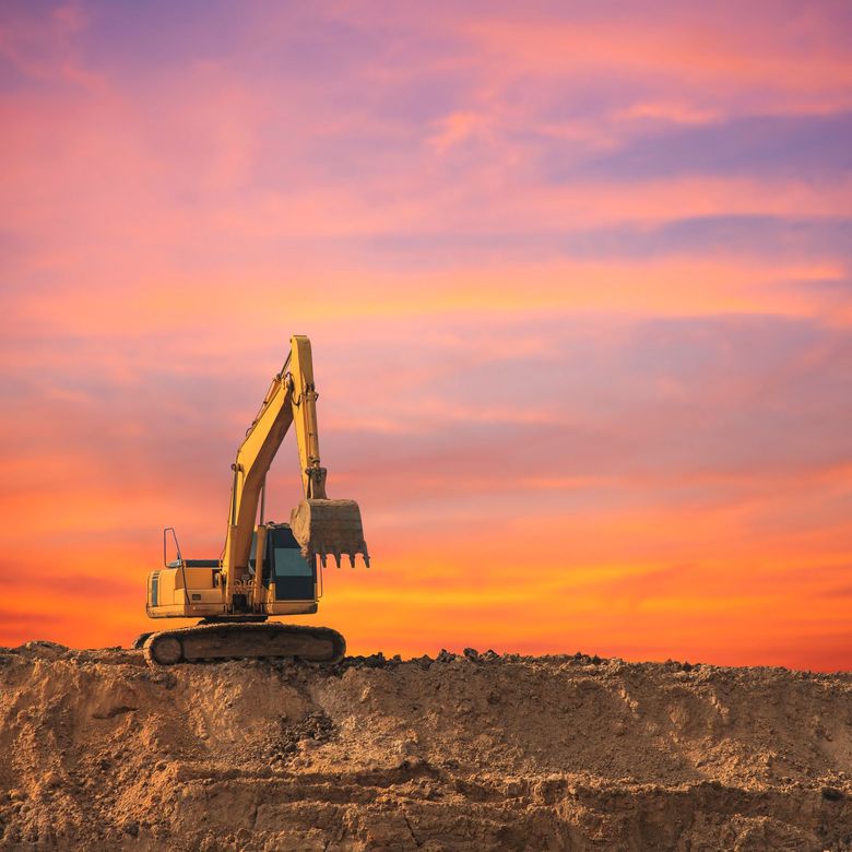 Yellow excavator loading dirt into a red dump truck at a construction site under a blue sky