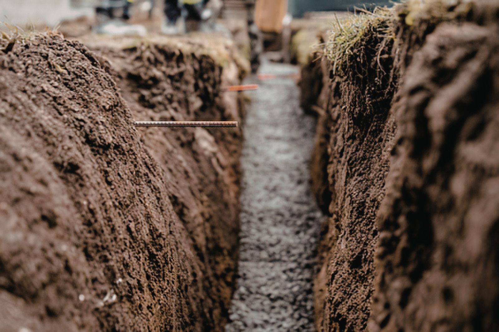 Narrow trench cut into brown soil, with rough dirt walls and blurred background