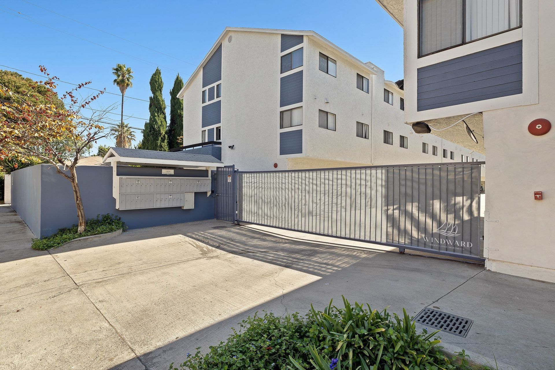 Apartment complex driveway with metal gate, concrete courtyard, and beige buildings under a blue sky