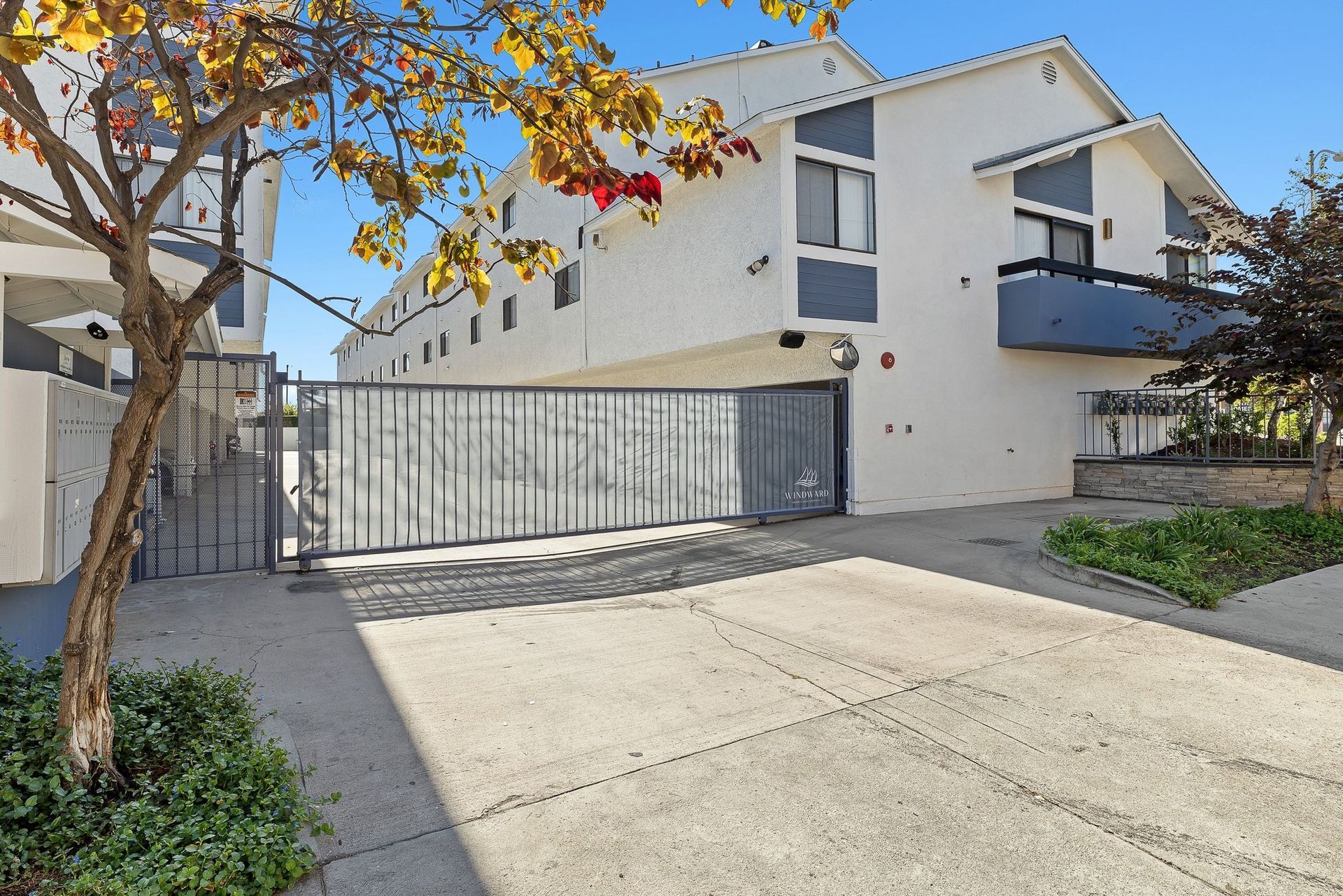 Apartment building with gated driveway, concrete courtyard, and a tree casting shadows in sunlight