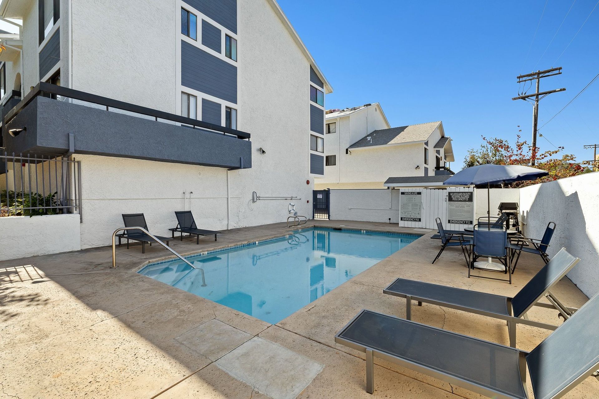 Apartment courtyard with a small blue swimming pool, lounge chairs, and a clear sky