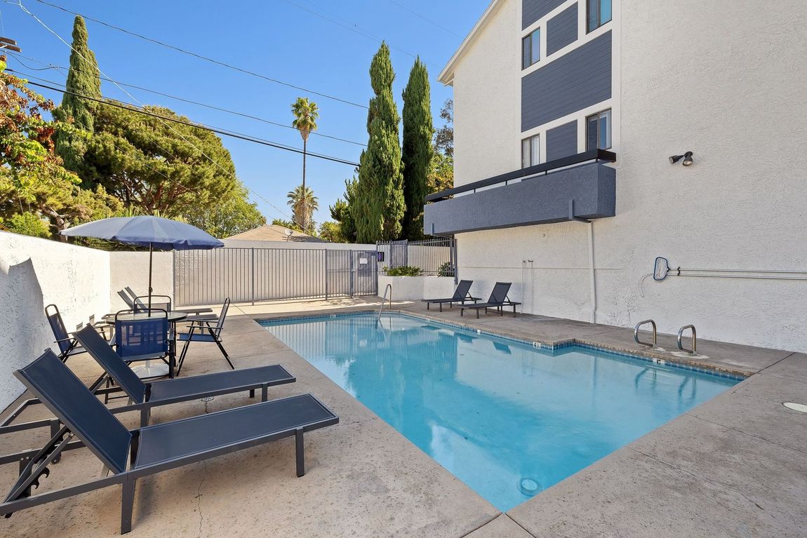 Backyard pool with lounge chairs, umbrella, and a modern house wall on a sunny day