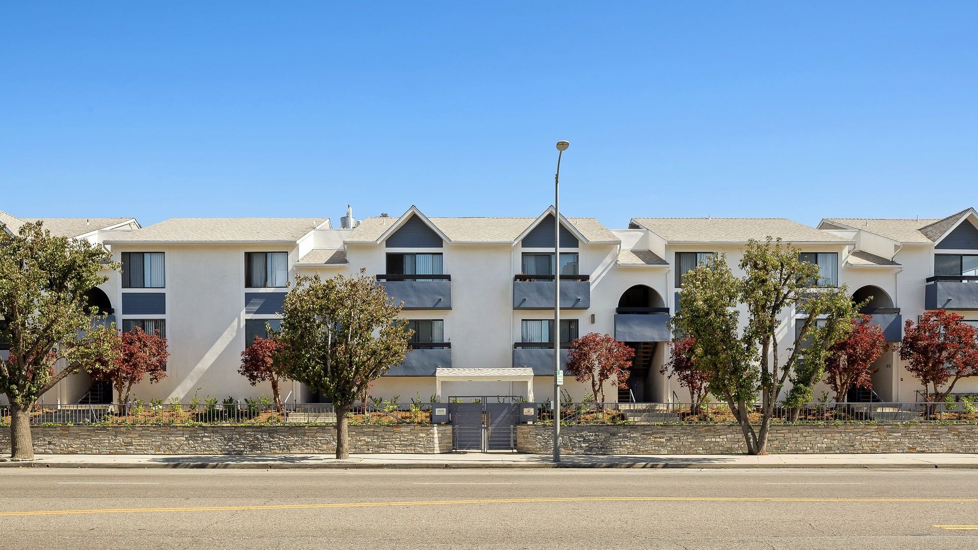 Apartment complex with white facades and trees along a roadside under a clear sky