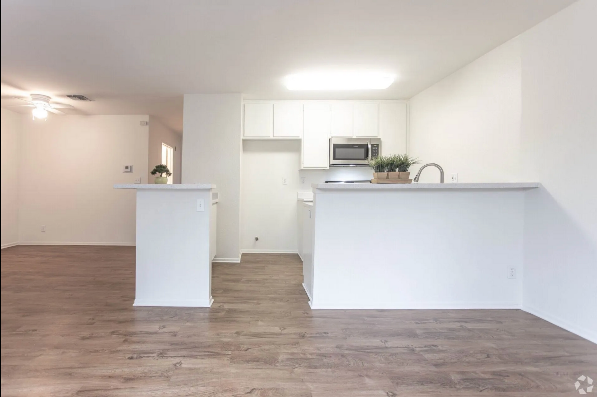 Bright open kitchen and living area with white counters, wood floors, and ceiling fan