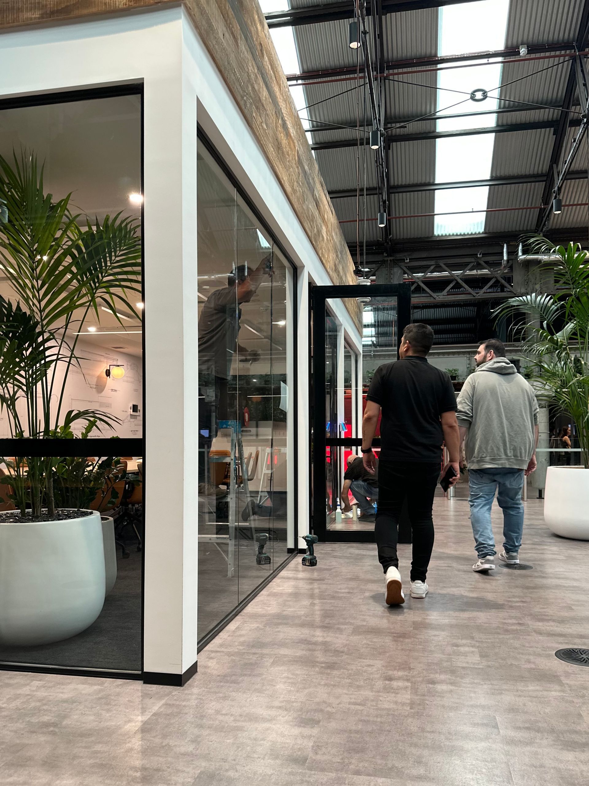 Two Men Walk Past a Glass-walled Office With Plants — All Glass Balustrading Systems in Wetherill Park, NSW