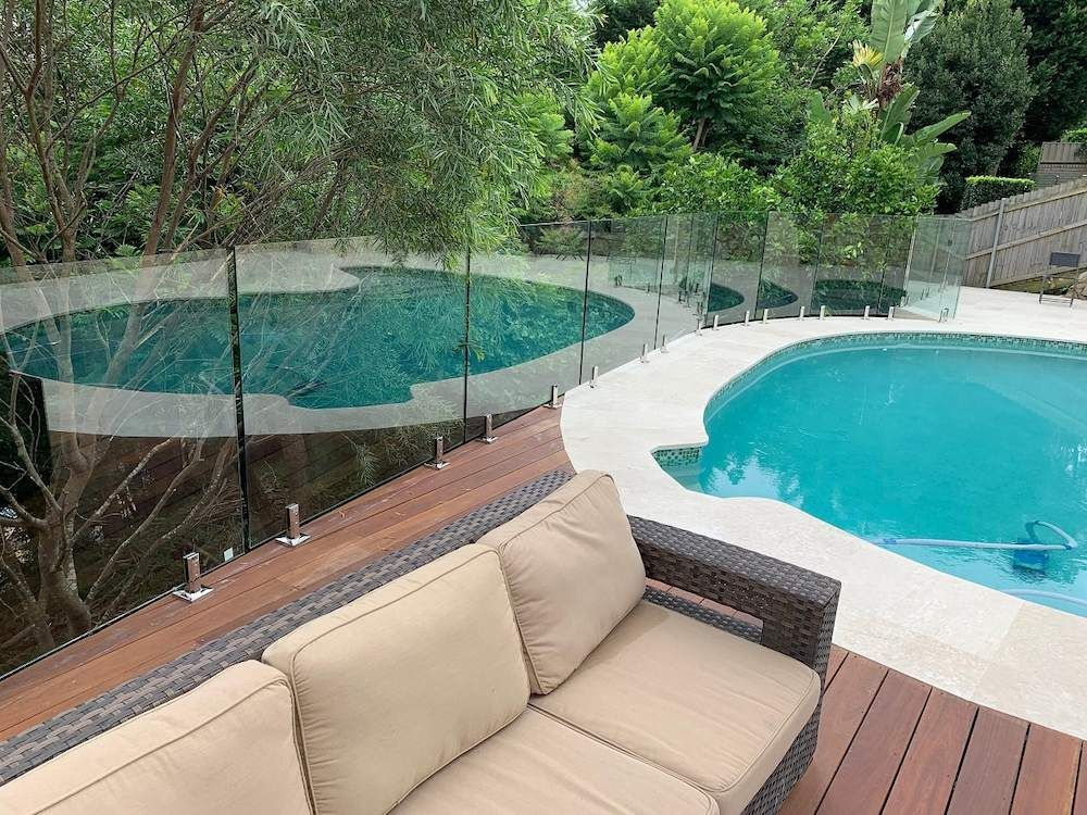 A Couch is Sitting on a Deck Next to a Swimming Pool — All Glass Balustrading Systems in Bondi, NSW