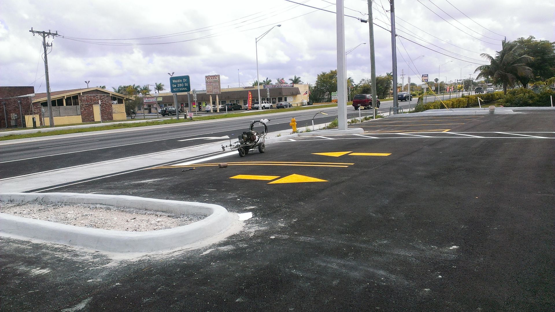 A road construction site with freshly painted yellow arrows on asphalt near a curb.