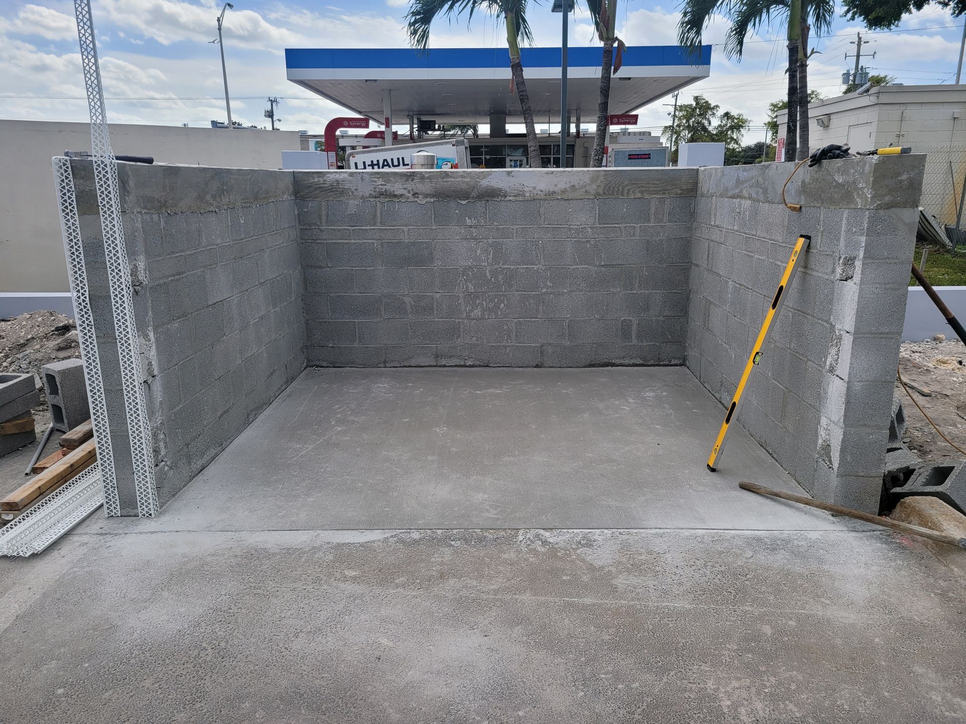 A U-shaped structure of gray cinder block walls built on a concrete slab, with a yellow level leaning against the right wall.