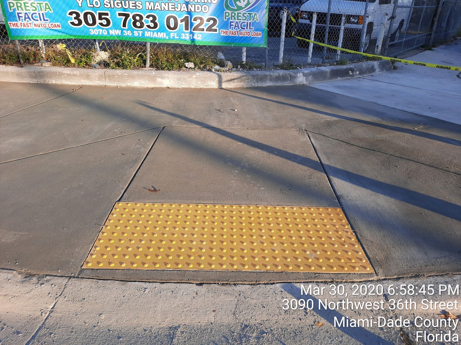 A yellow truncated dome tactile paving mat set into a concrete sidewalk at a curb ramp in Miami-Dade County.