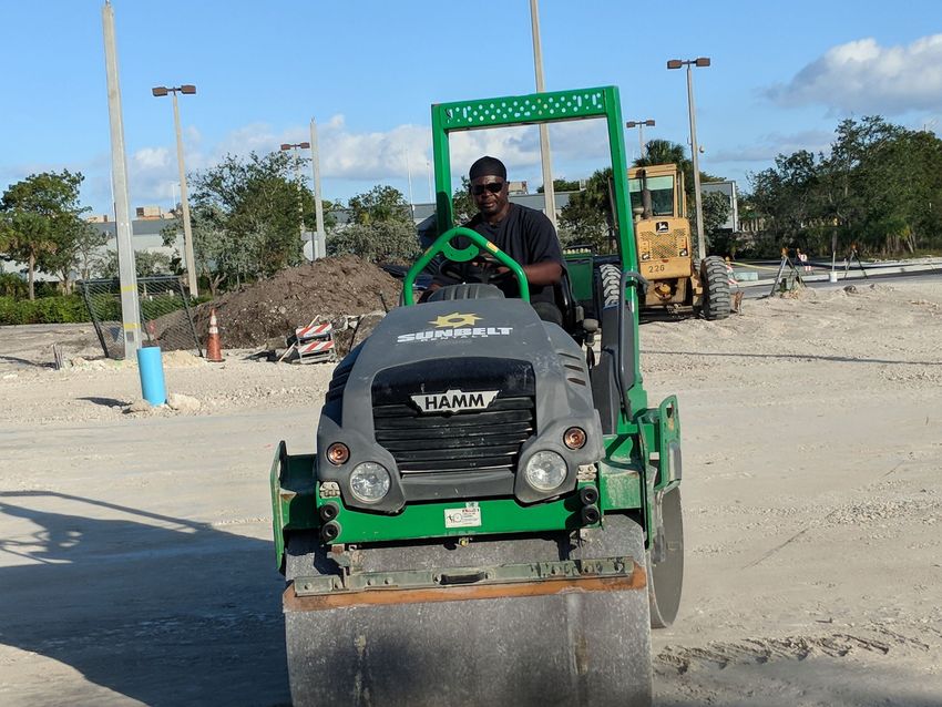 Construction workers smoothing wet concrete with a power trowel at a job site with machinery in the background.