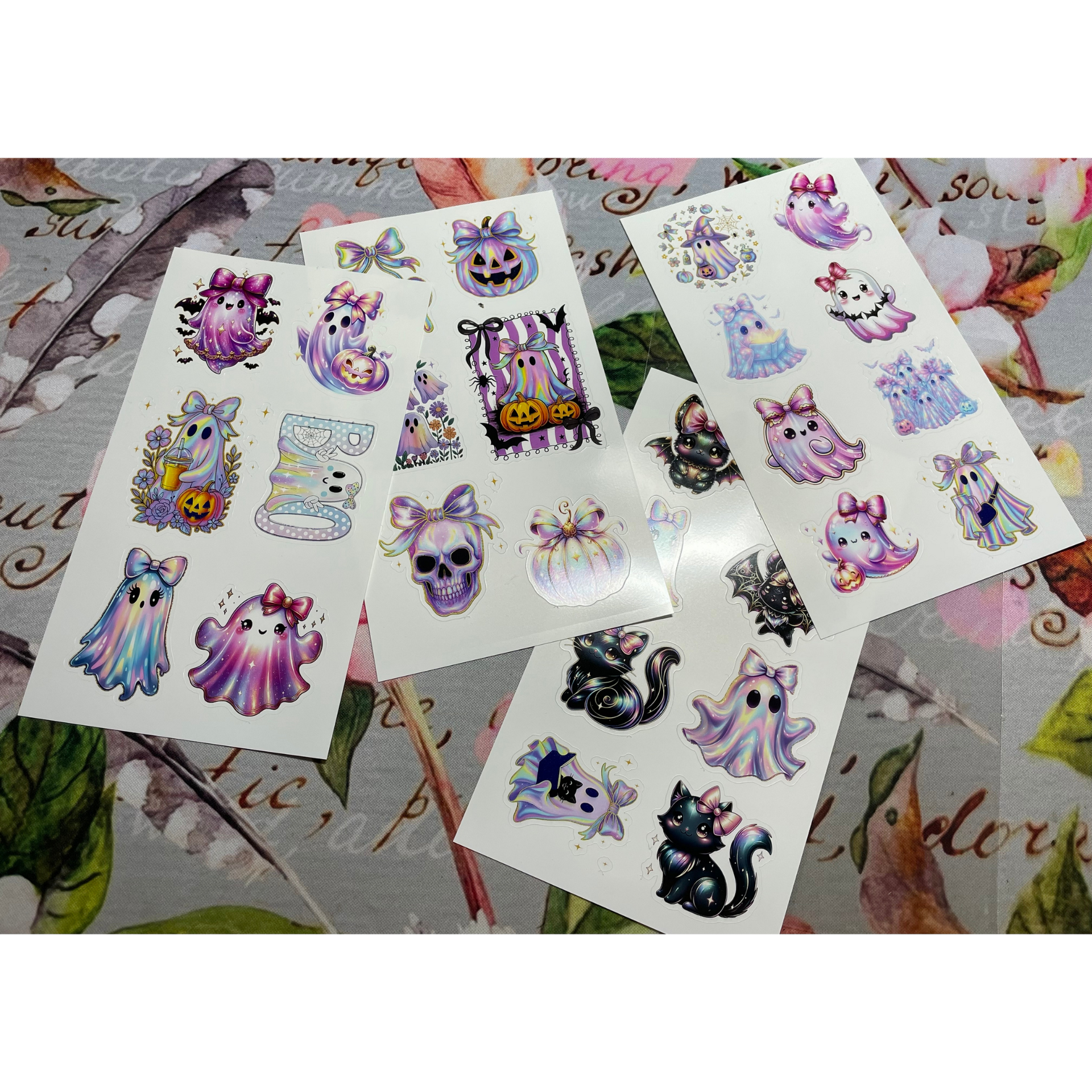 Assorted pastel spooky-cat sticker sheets spread on a floral surface