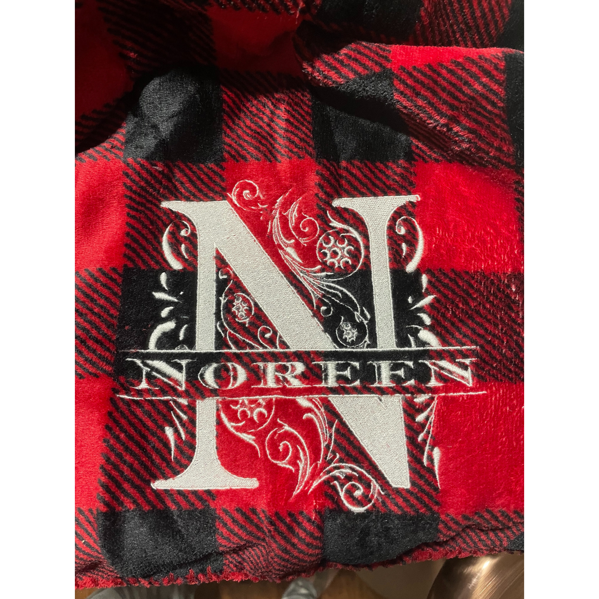 Red and black plaid fabric with a large ornate white letter N and the word “Norelyn” across it