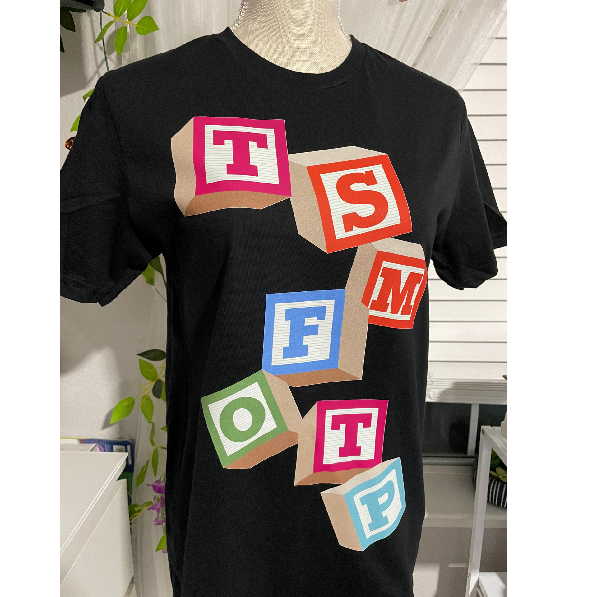 Black T-shirt with colorful block letters spelling “STOFM” on a mannequin.