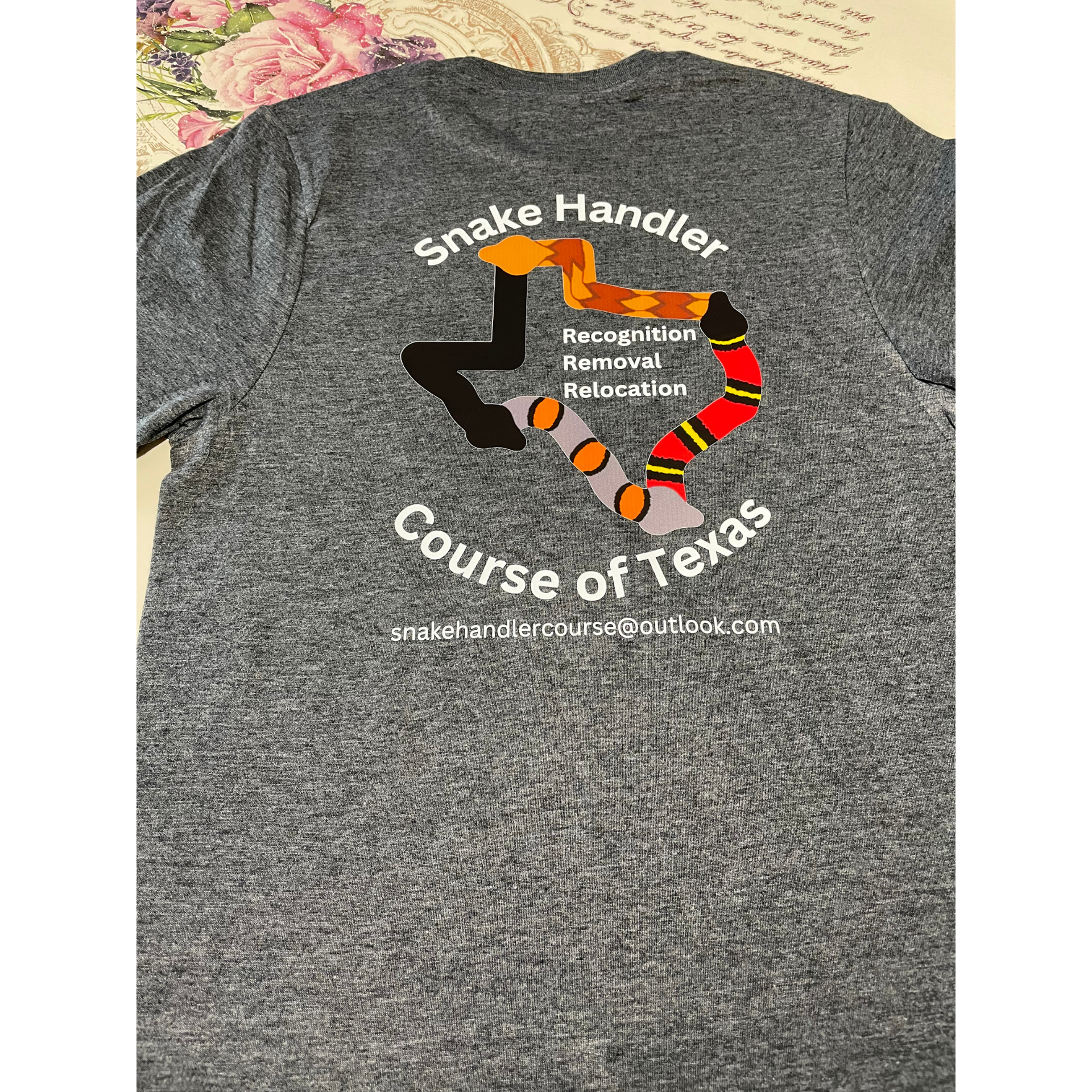 Gray T-shirt with a Texas snake graphic and curved text reading “Snake Handler” and “Course of Texas”
