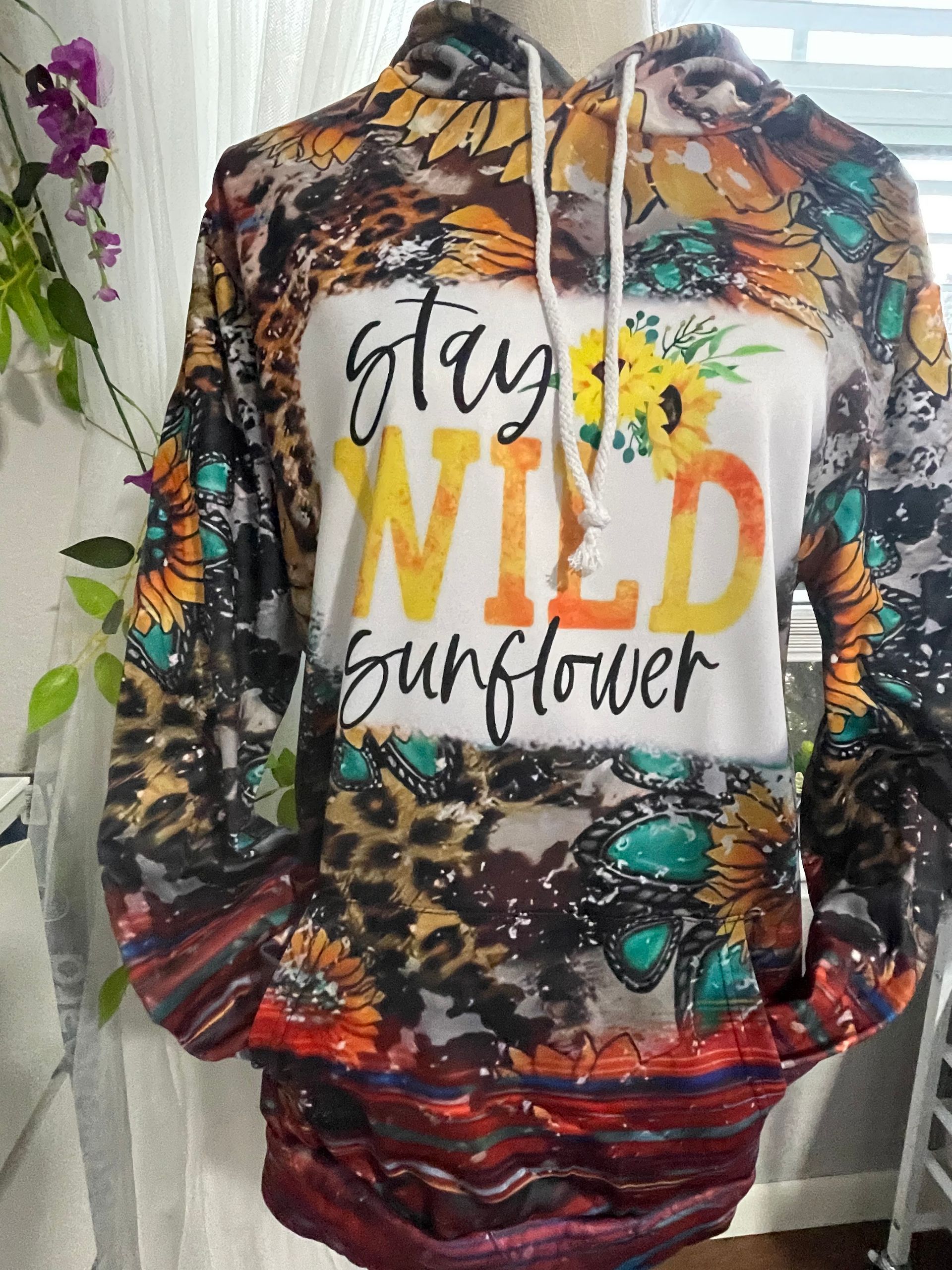 Colorful floral hoodie with “stay wild sunflower” text, hanging on a rack indoors