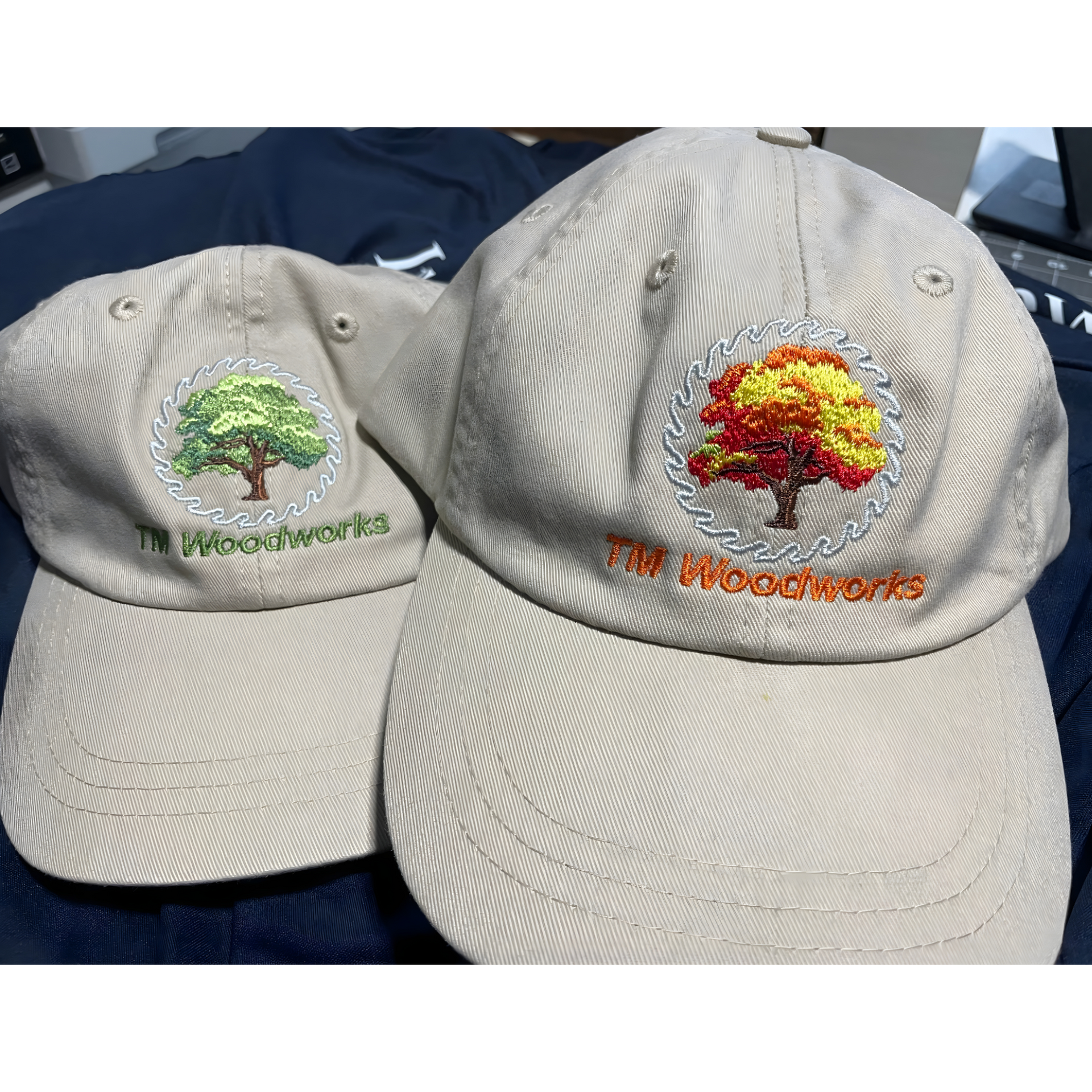 Two beige baseball caps with embroidered trees, one green and one red-orange, on a dark blue surface