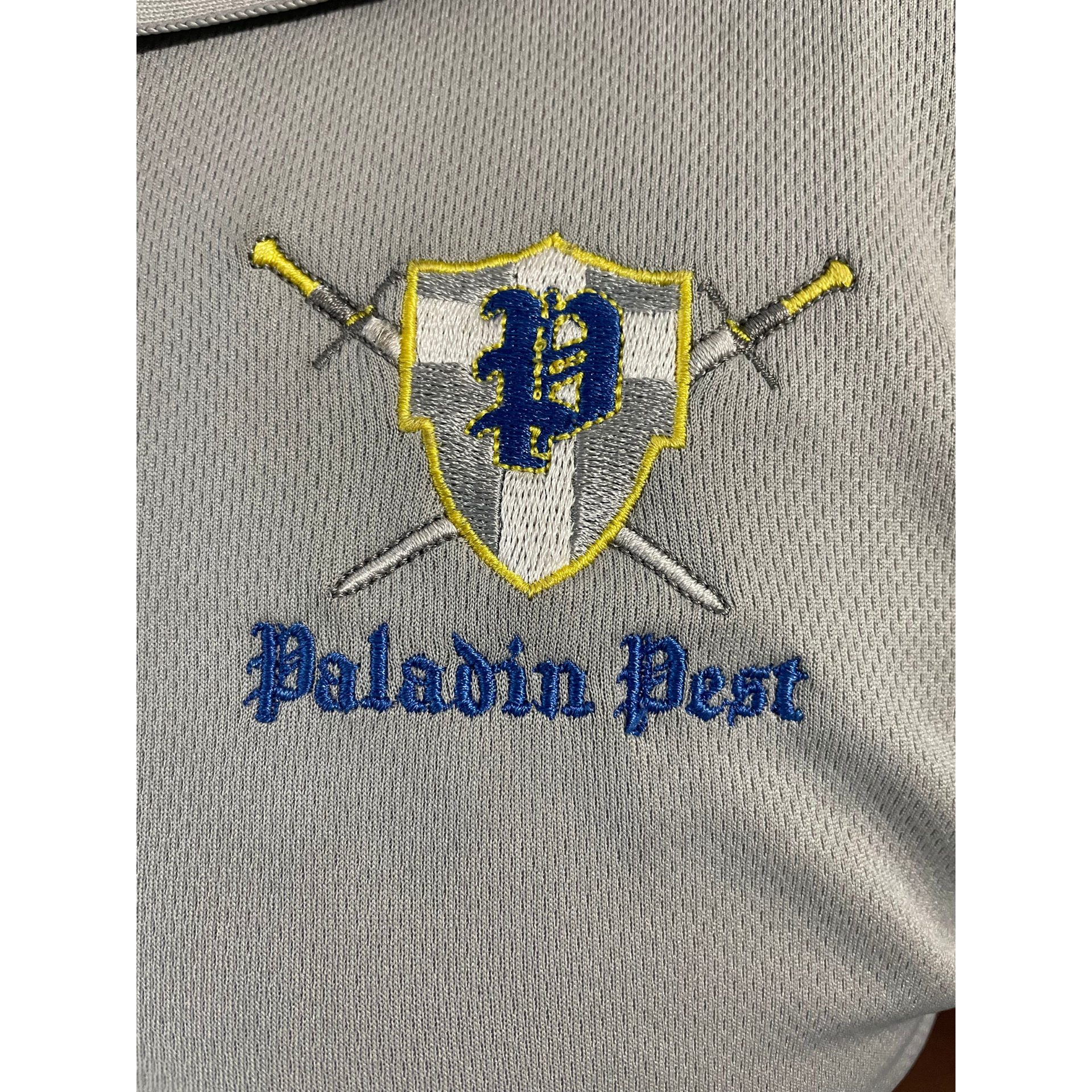 Gray shirt with a yellow-trimmed shield crest, crossed swords, and blue “Pelham Pest” text