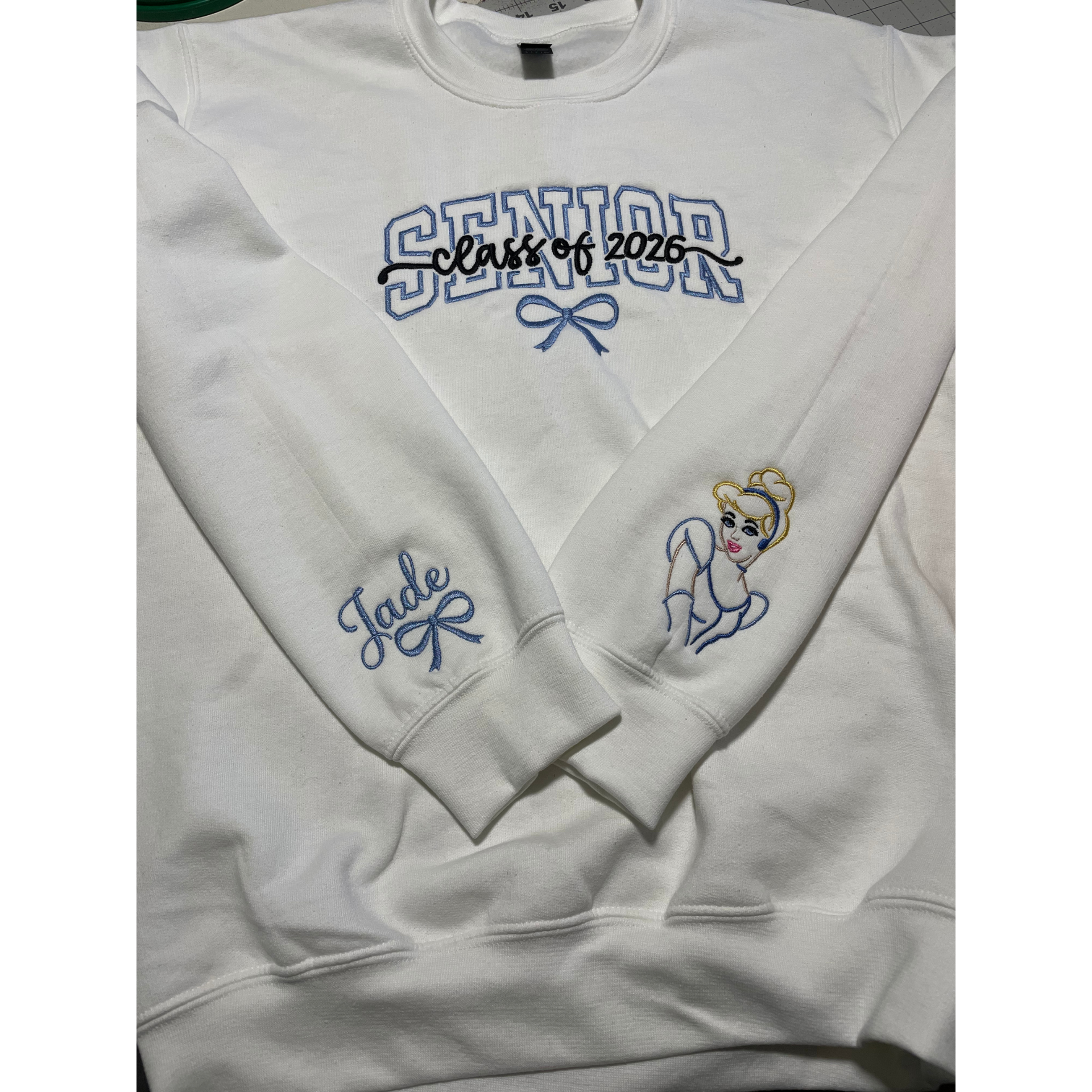 White sweatshirt with blue “Class of 2025” text, “Julie” on sleeve, and a small bride illustration.