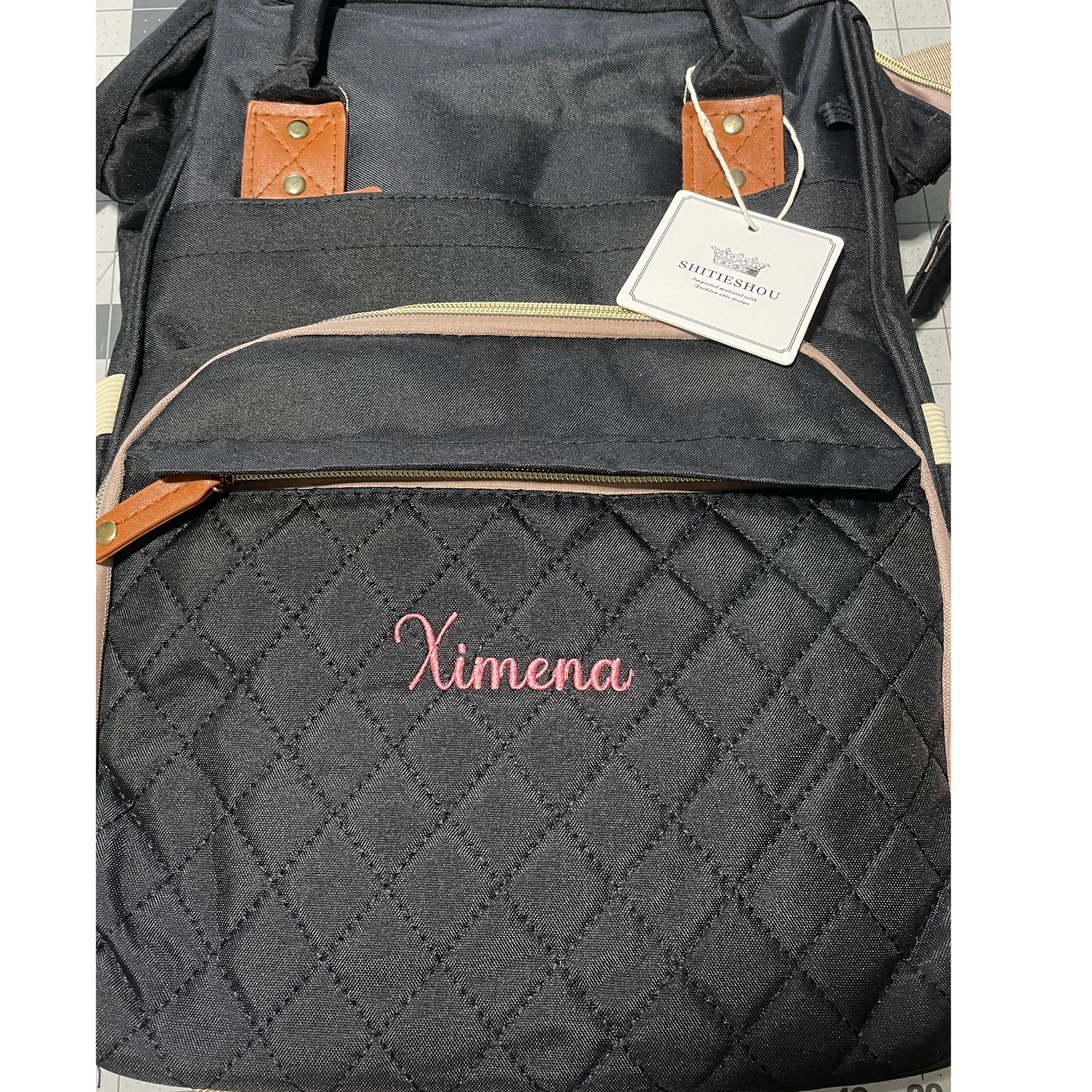 Black textured Ximena handbag with tan accents and a hanging tag, shown close up.