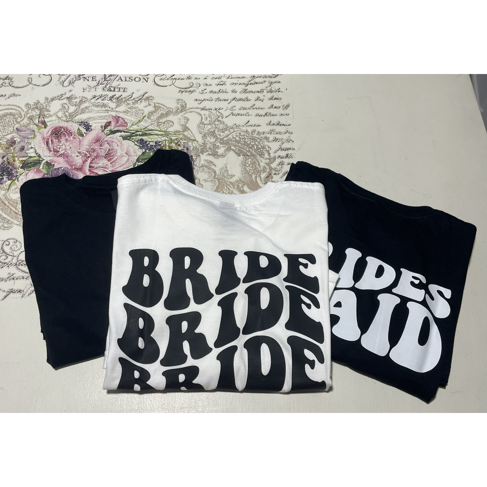 Three folded T-shirts with bold black and white BRIDE text on a table