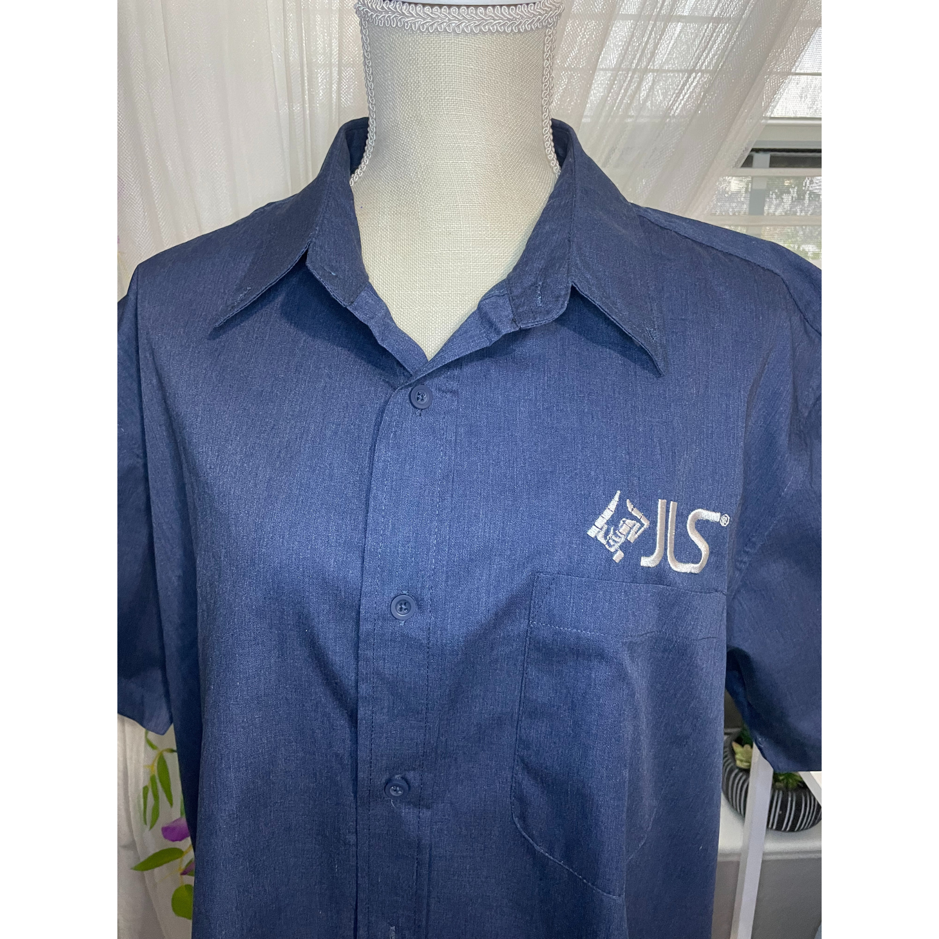 Blue collared shirt on a mannequin, with white embroidered lettering on the chest.